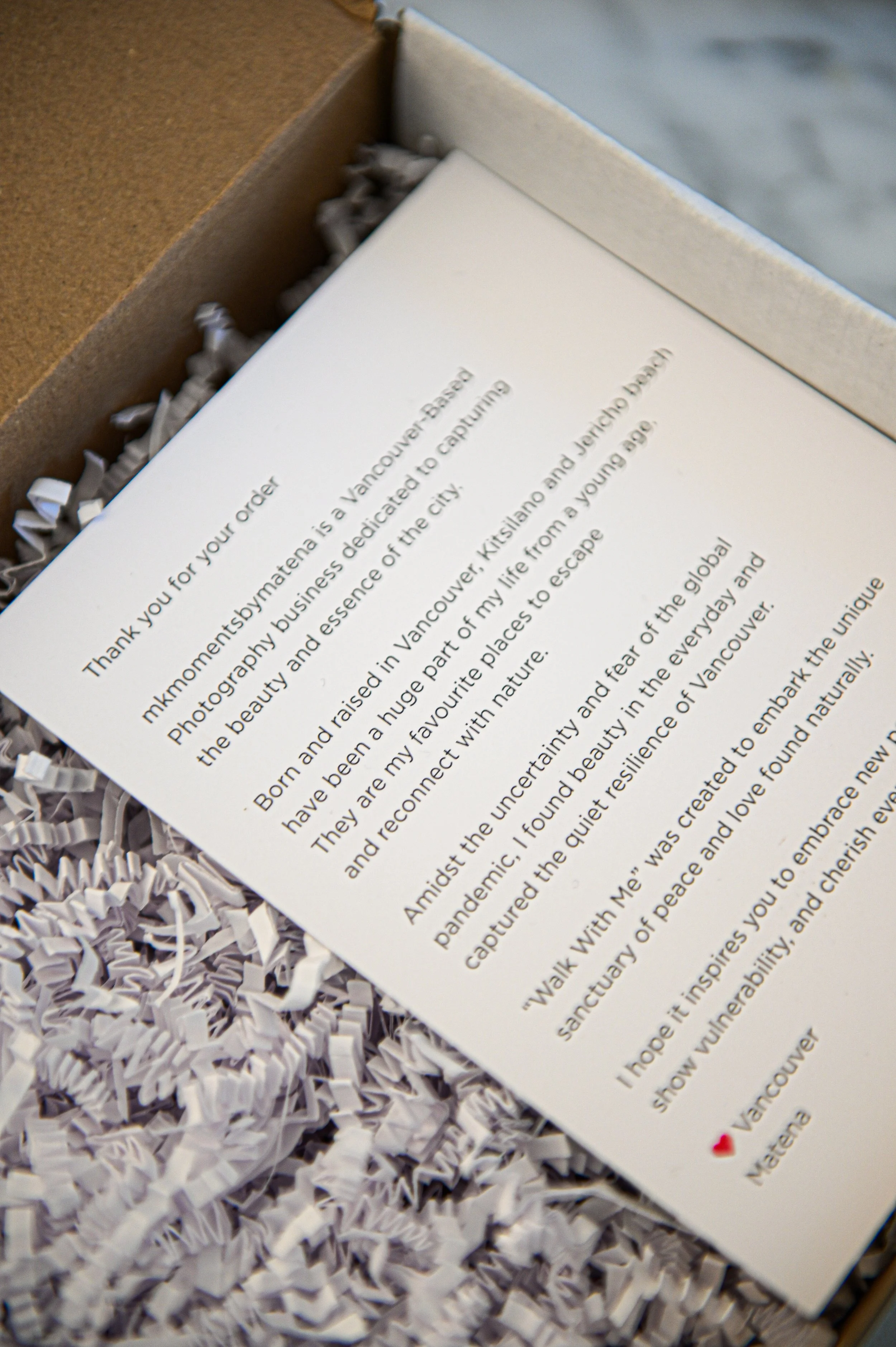 Close-up of a printed letter on white paper inside a cardboard box filled with shredded paper, with a gray stone surface in the background.