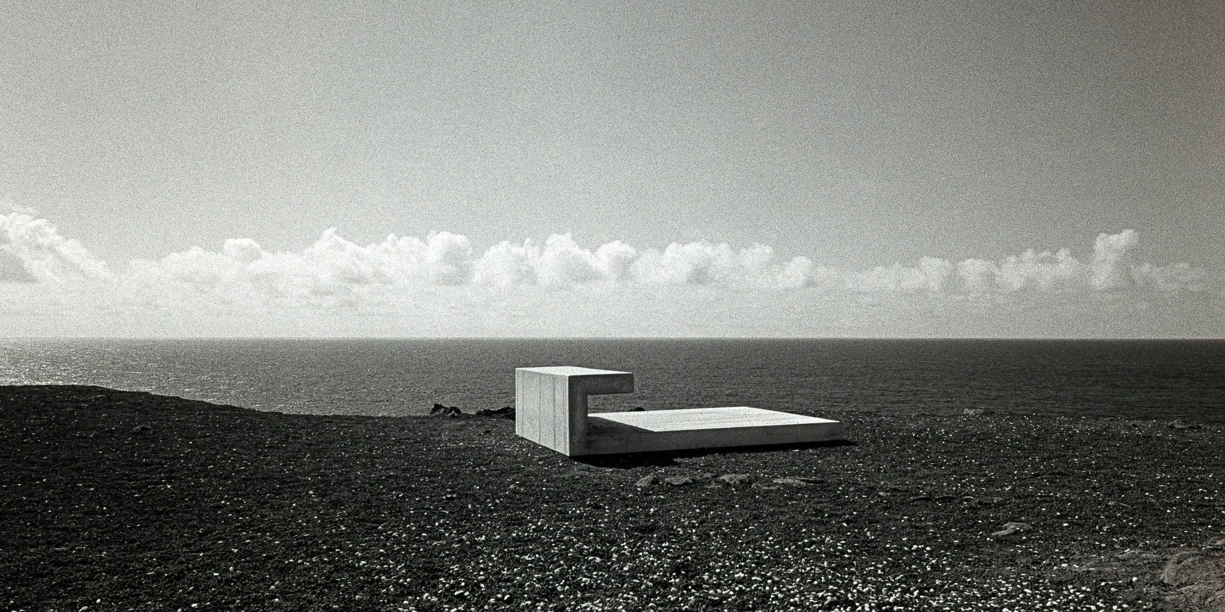 Minimalist black and white analog photograph of a concrete geometric structure on a dark volcanic beach horizon by Donatas Berlinskas
