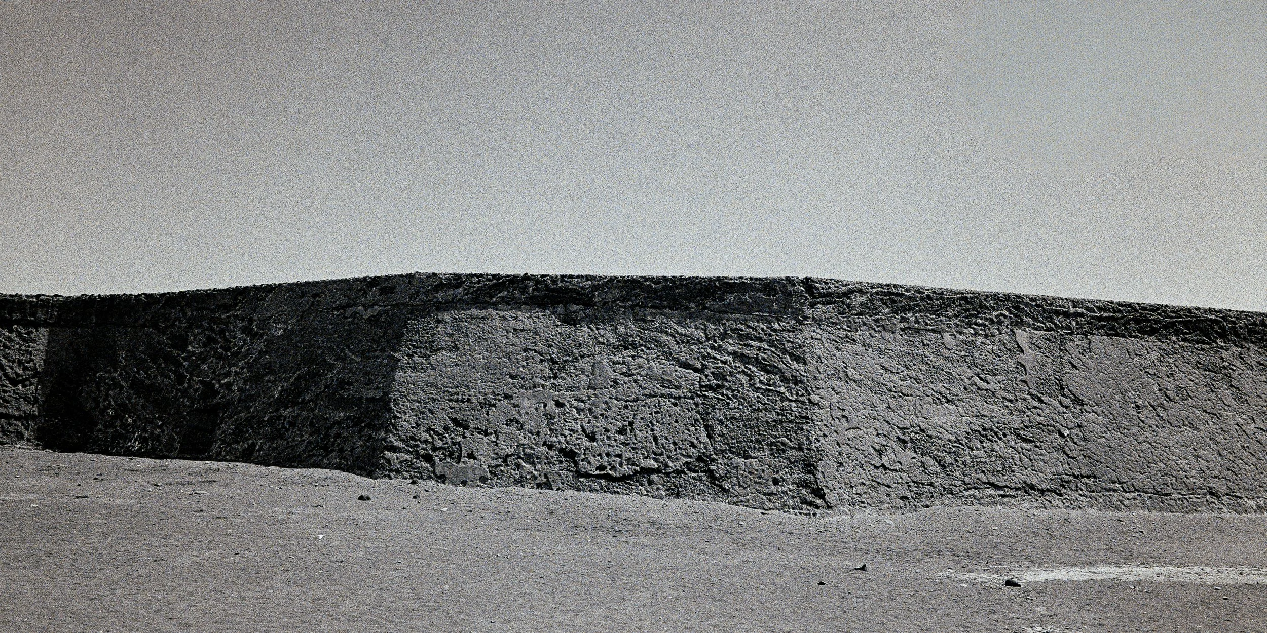 Minimalist black and white analog photograph of a long concrete structure dividing an open landscape by Donatas Berlinskas