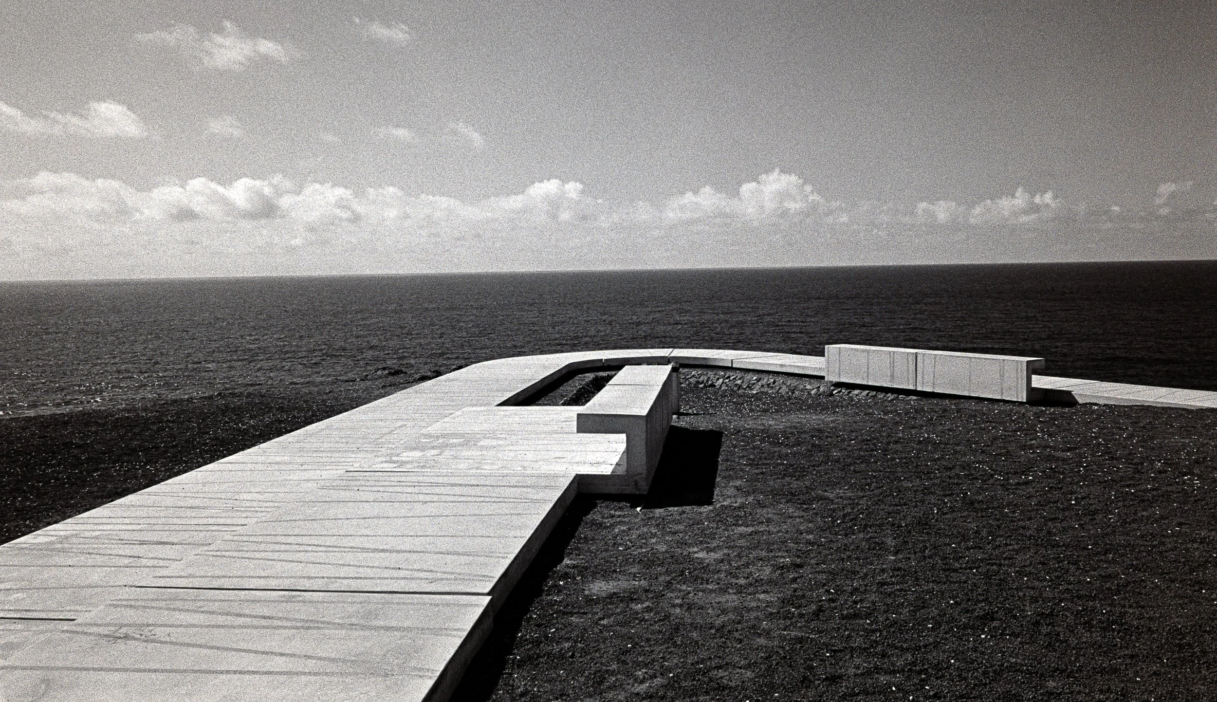 Minimalist black and white analog photograph of a geometric concrete pier extending toward the sea horizon by Donatas Berlinskas