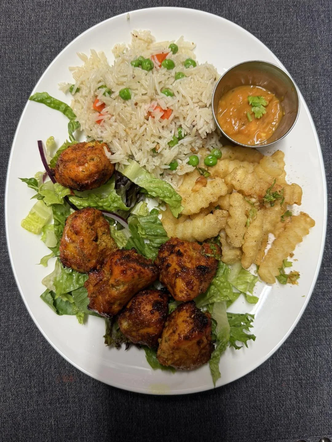 Plate of Indian cuisine with rice, fried chicken pieces, vegetable salad, and a small bowl of curry or sauce.