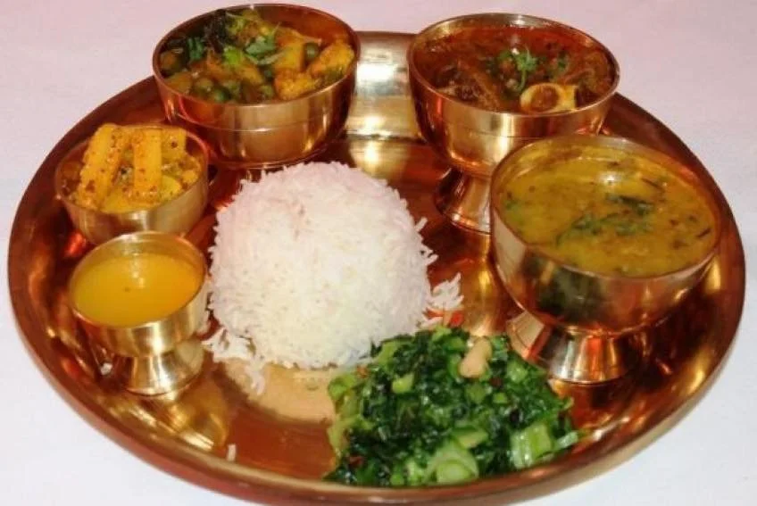 A traditional Indian Thali with rice, dal, vegetable curry, sambar, rasam, and mixed greens on a copper tray.