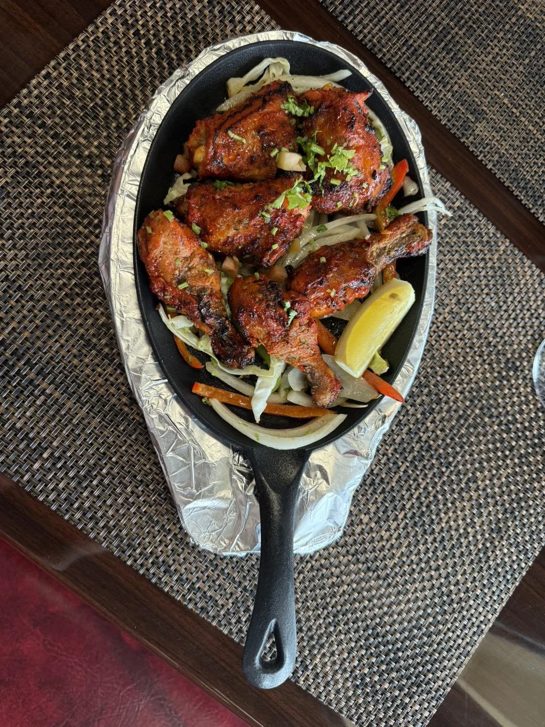 Grilled chicken drumsticks and thighs with vegetables and lemon wedge on a sizzling platter