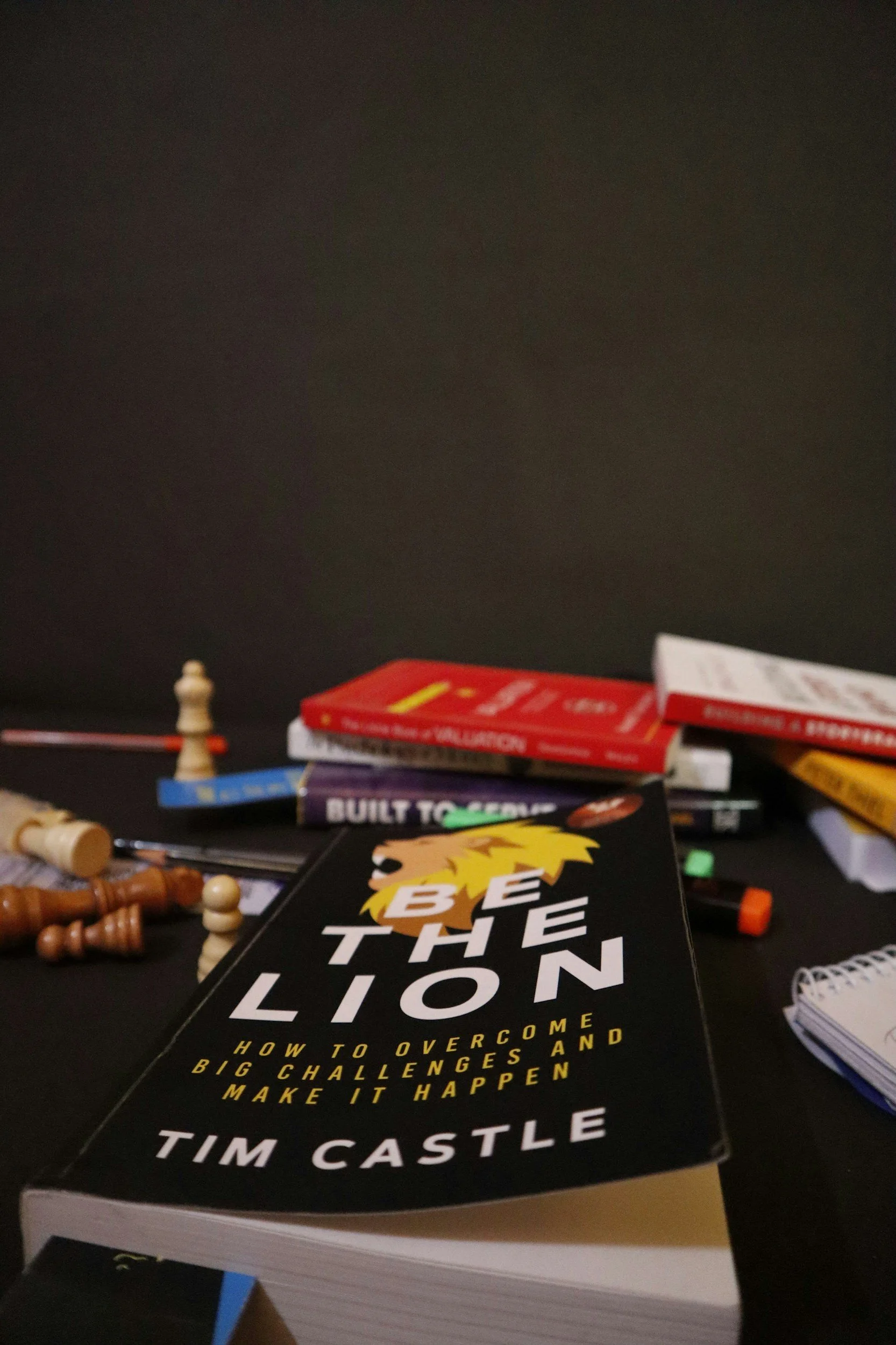 Varios libros y piezas de ajedrez en una mesa, con un fondo oscuro.