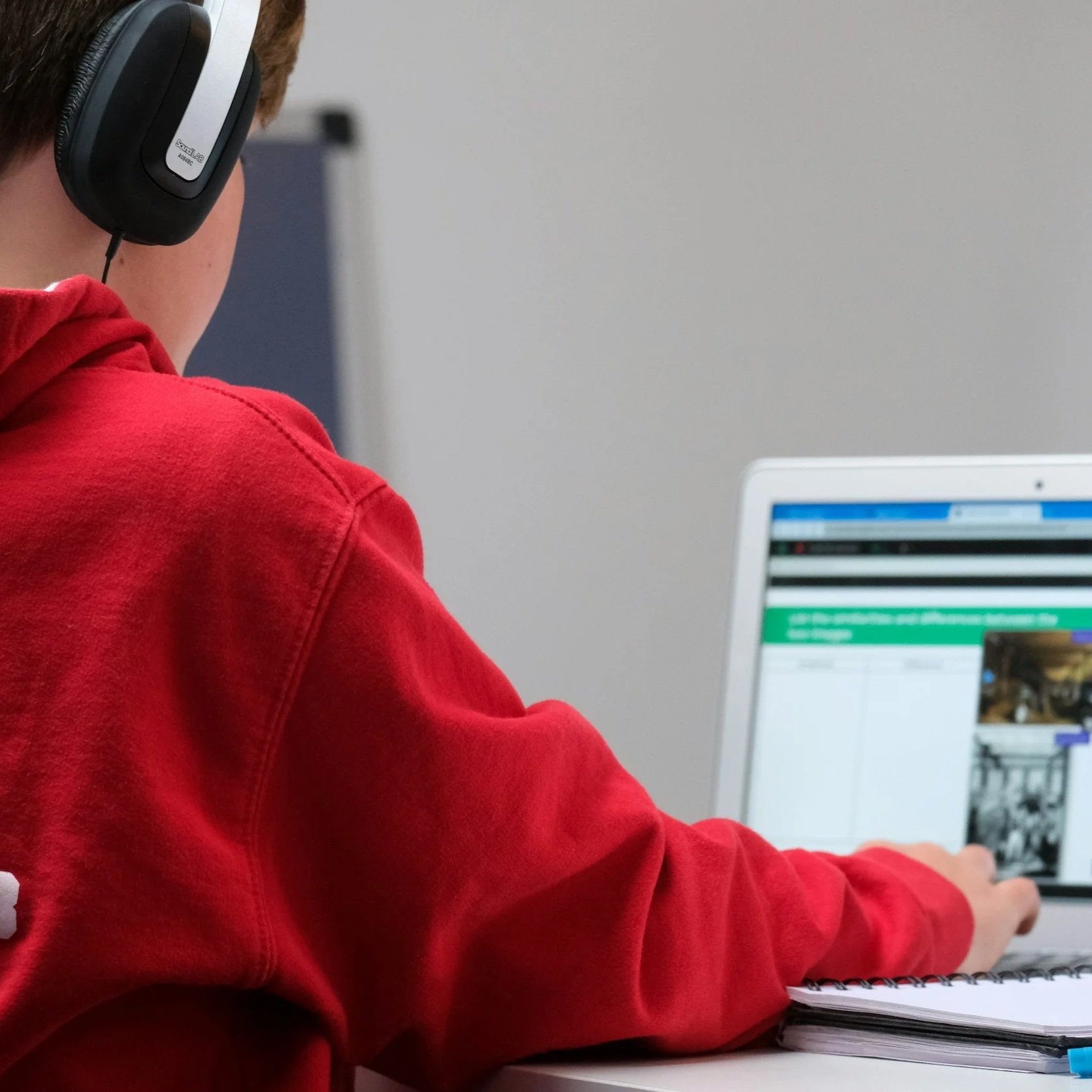 Persona con sudadera roja usando audífonos trabajando en una computadora en una oficina.