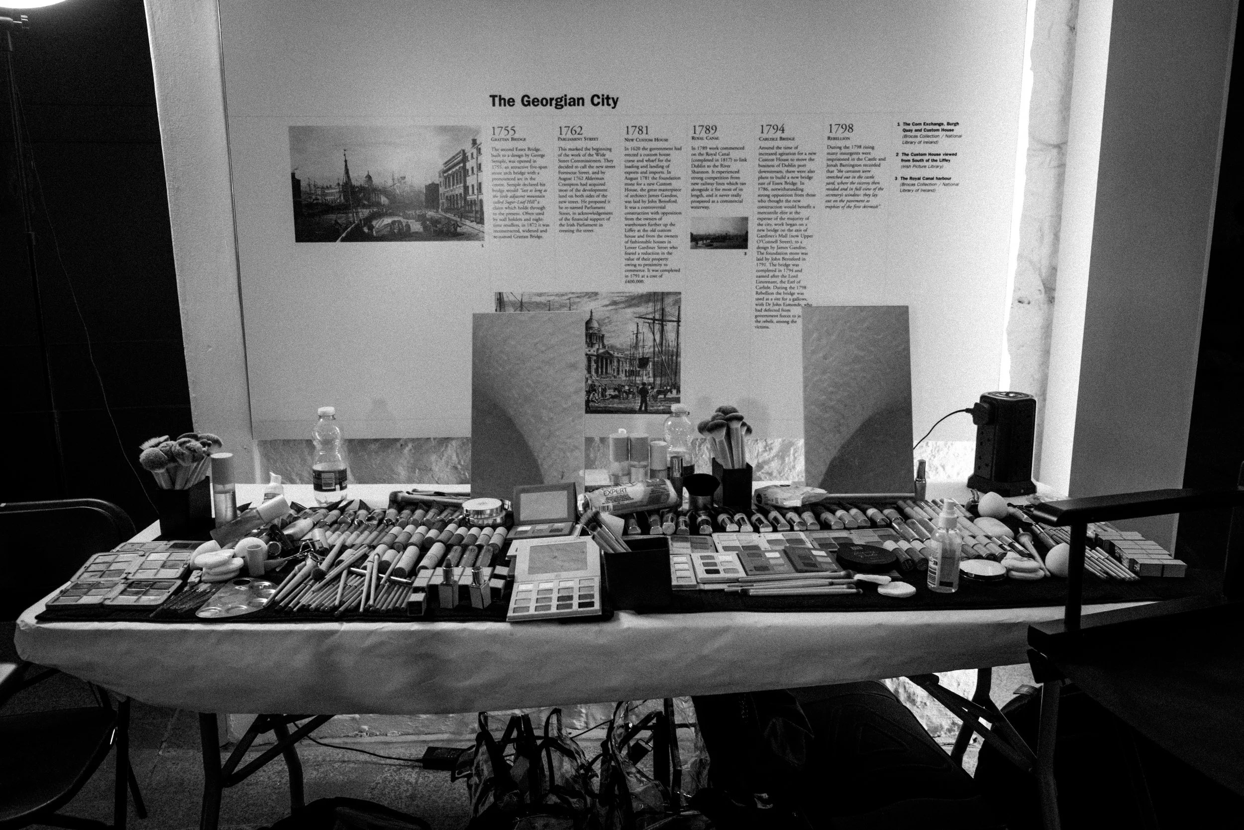 Art supplies and makeup products arranged on a table in front of an informational display about the history of The Georgian City.