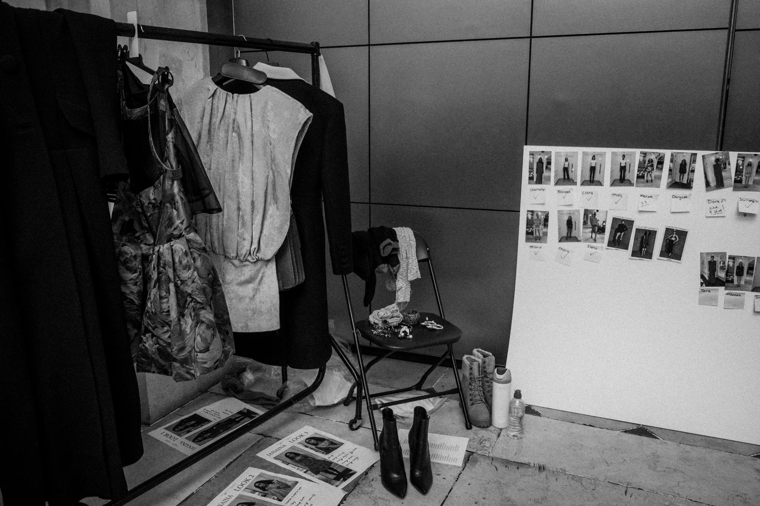 Fashion design workspace with clothing rack, dresses, photos on a whiteboard, shoes, water bottle, and accessories.