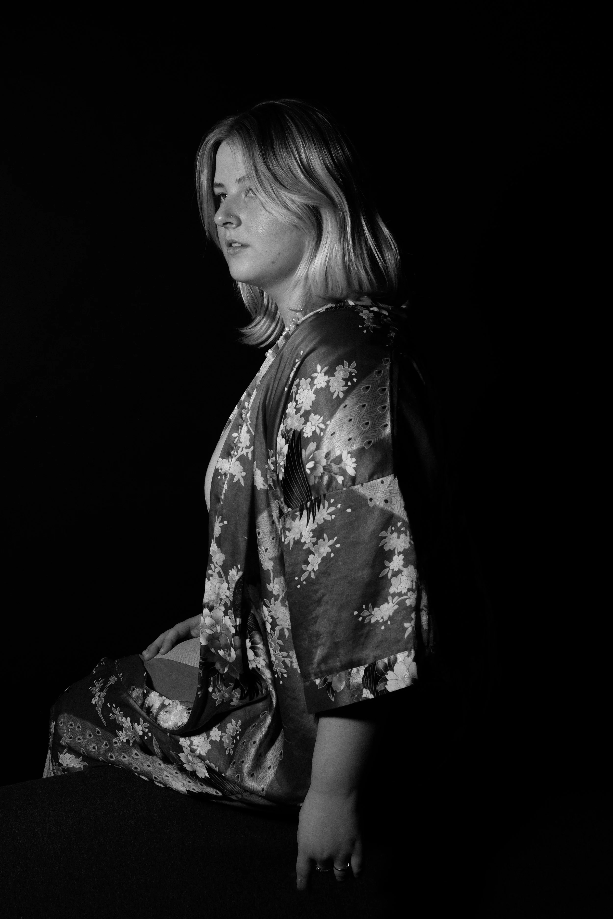 A black and white portrait of a woman with shoulder-length hair in a floral-patterned kimono, sitting against a dark background.
