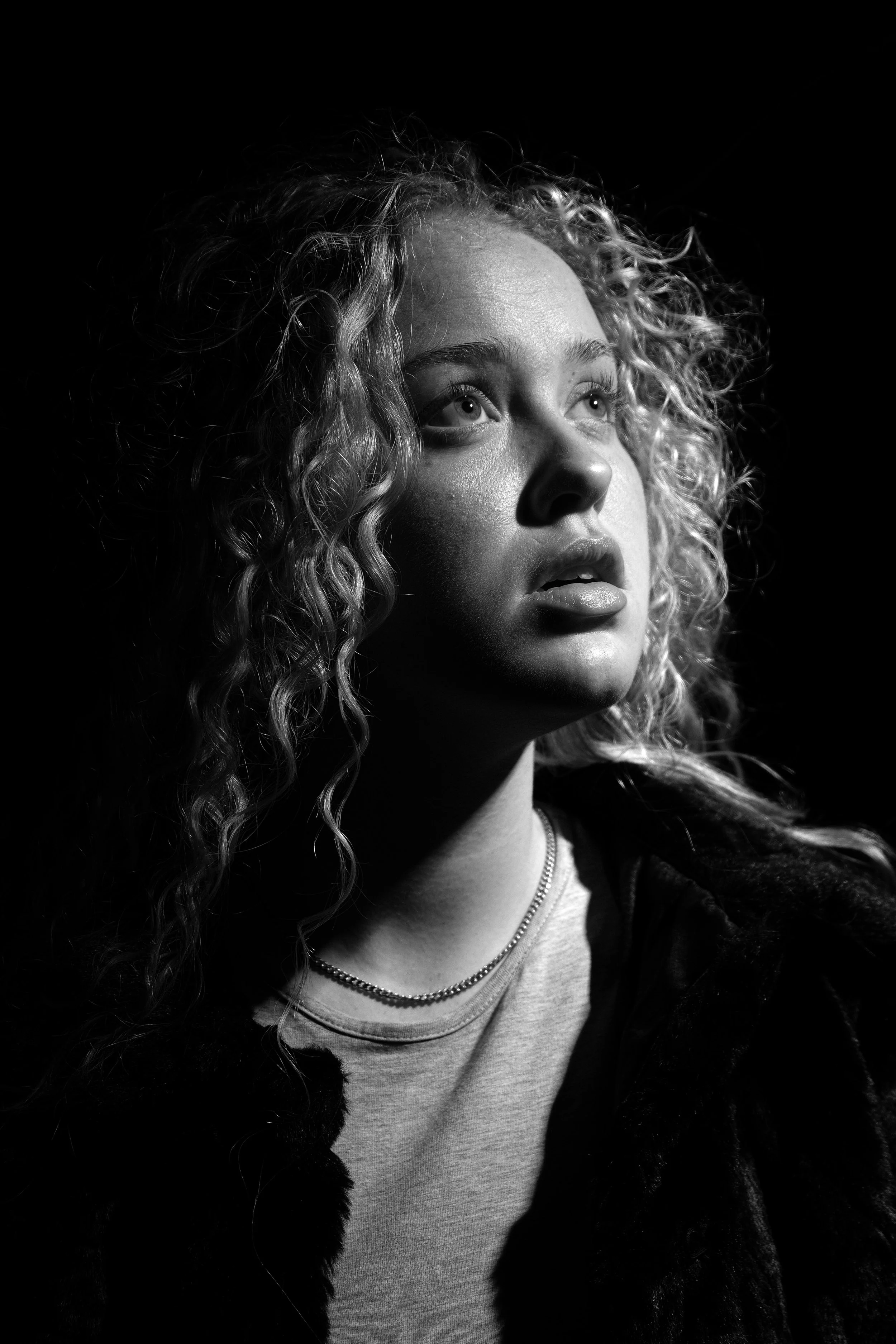 Black and white portrait of a young woman with curly hair, looking upward with a contemplative expression.