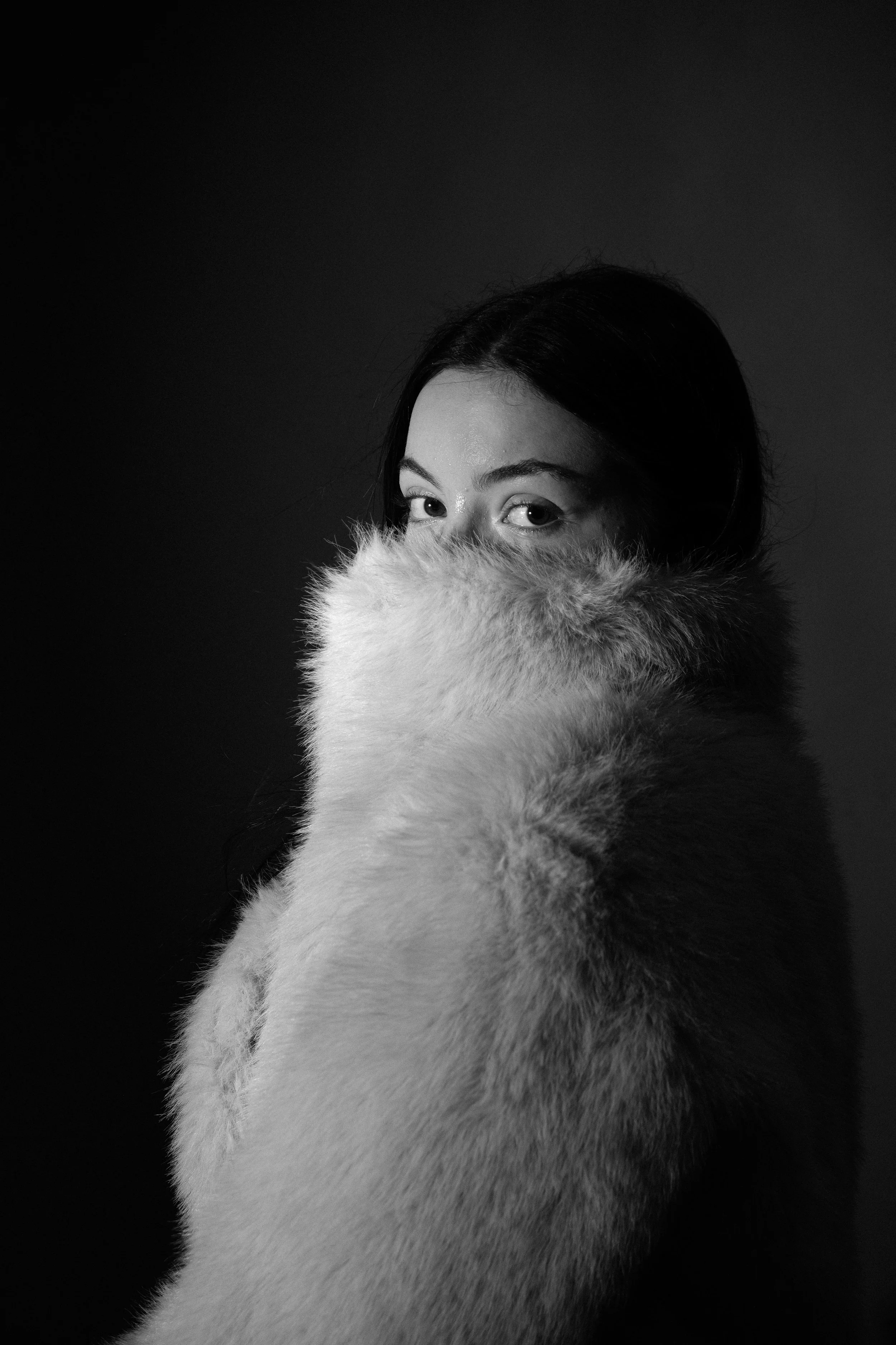 Black and white portrait of a woman partly covered with a fur coat, with only her eyes and hair visible.