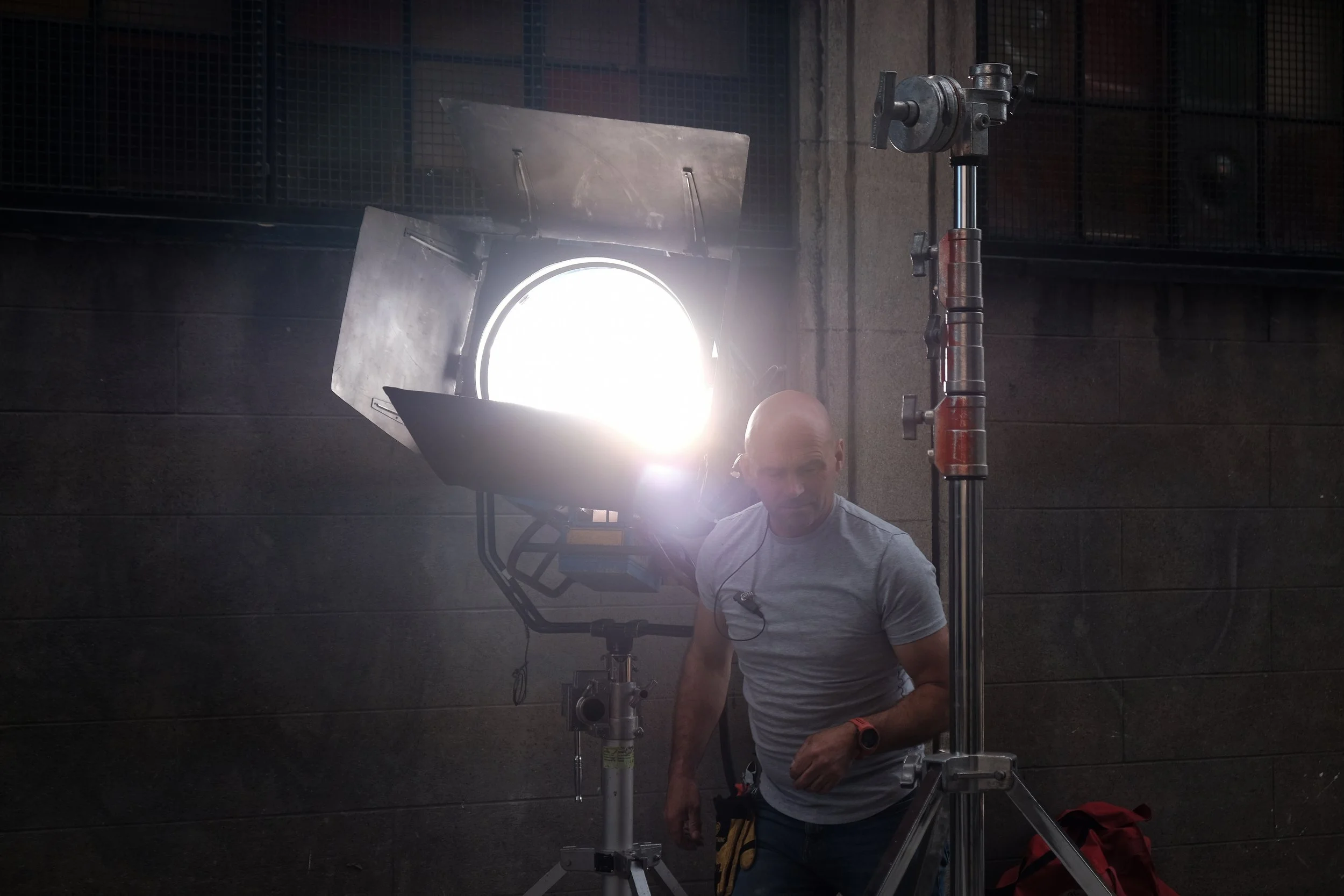 A man adjusting a film or photography light indoors with dark walls and a metal grid above.