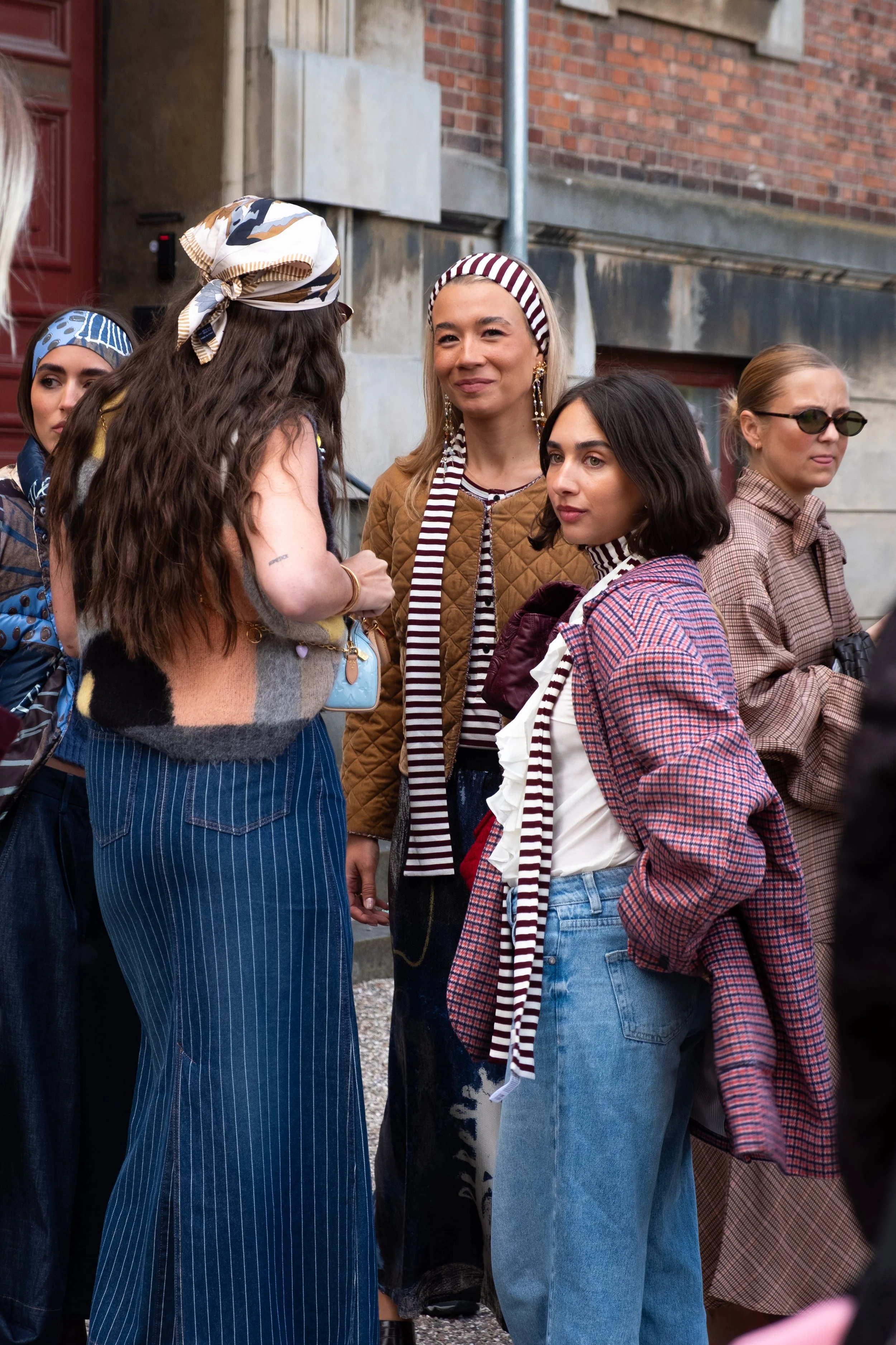 Group of women in fashionable clothing engaged in conversation outdoors on a city street.