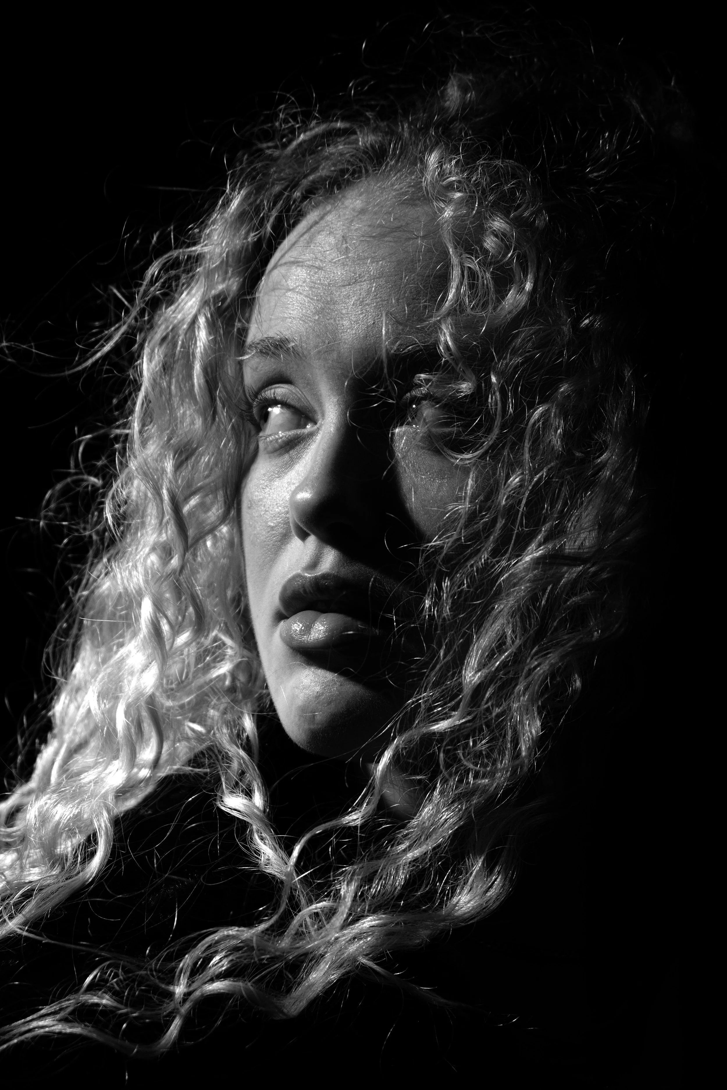 Black and white portrait of a woman with curly hair, looking to the side with a serious expression.