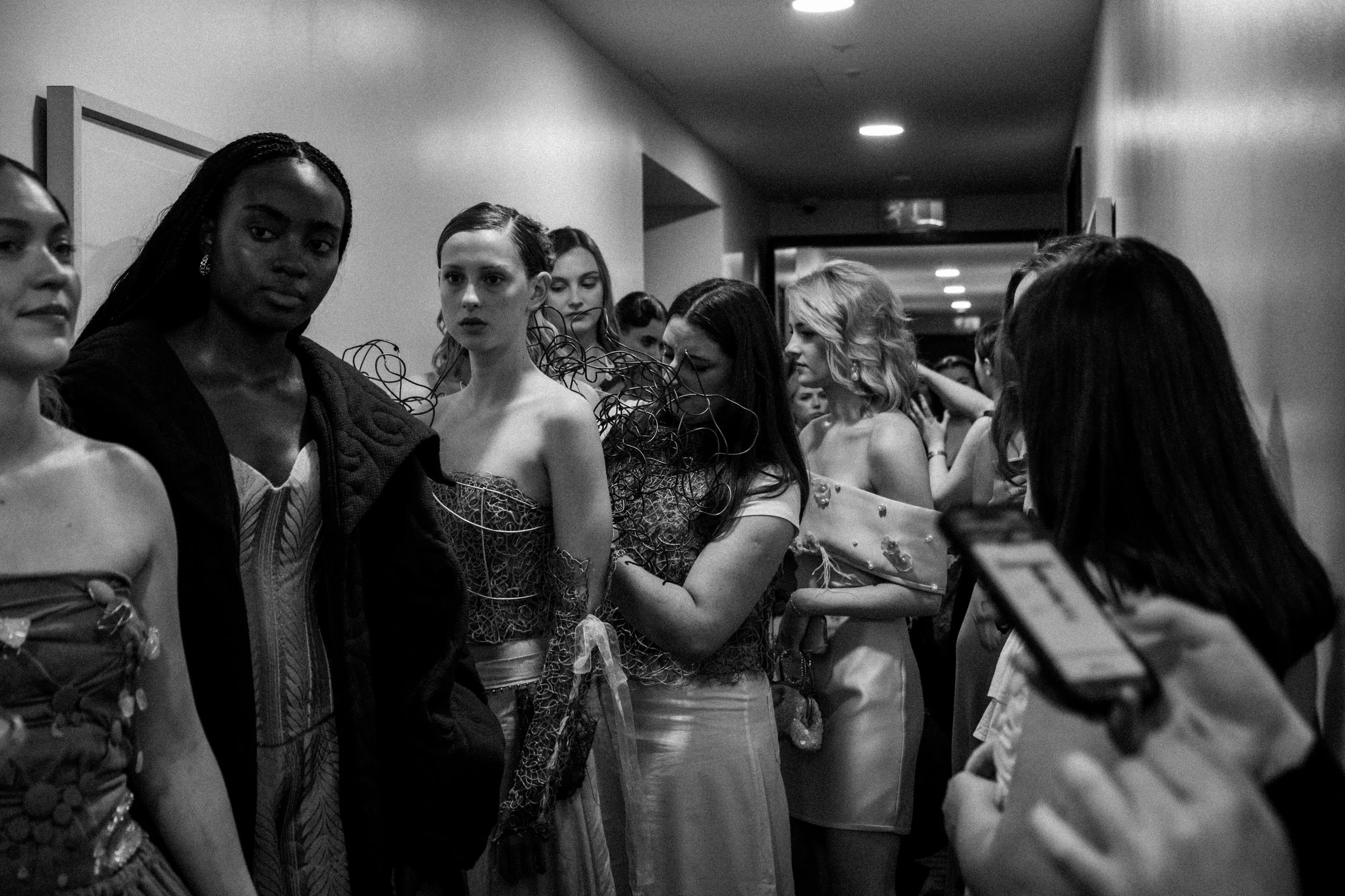 Women in an event hallway, some in elaborate fashion, waiting in line or observing.
