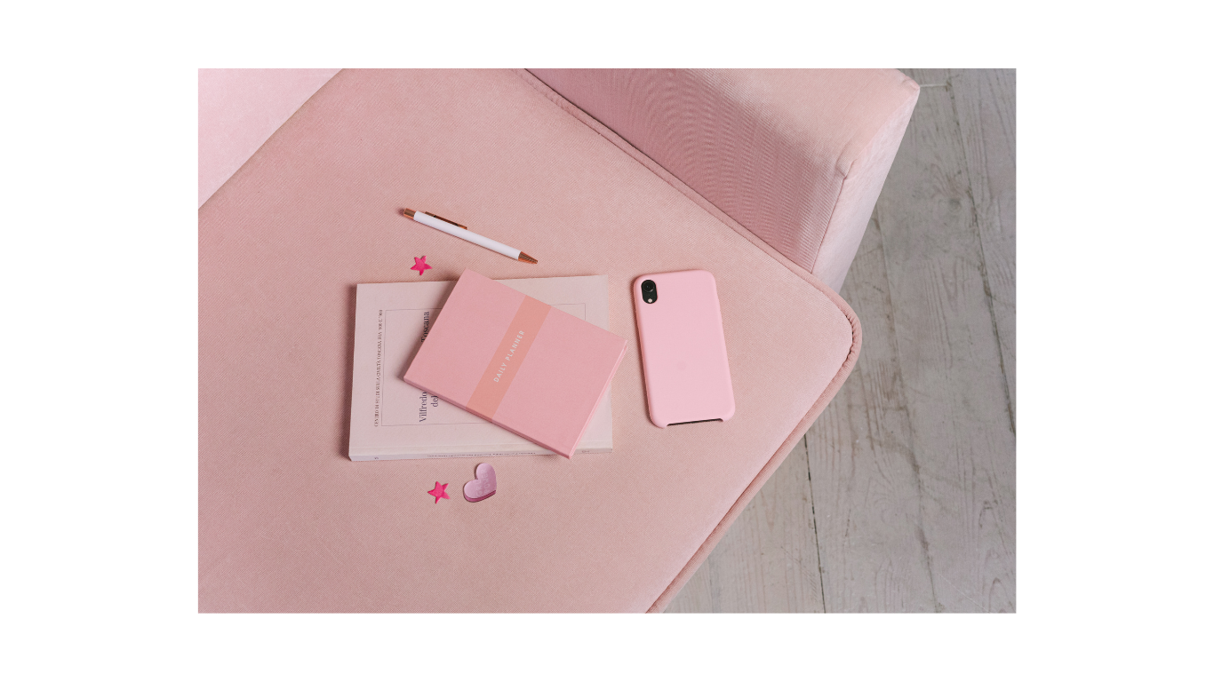 A pink armchair with a pink notebook, a book, a pink phone, a white pen, and small pink star and heart stickers on the seat.