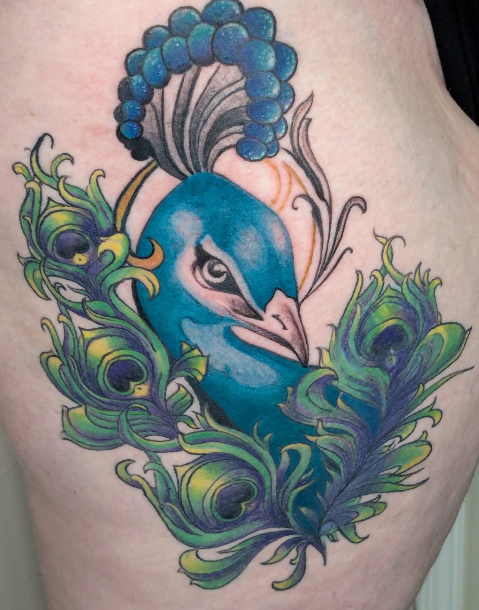 Colorful blue peacock tattoo with green and purple feathers.