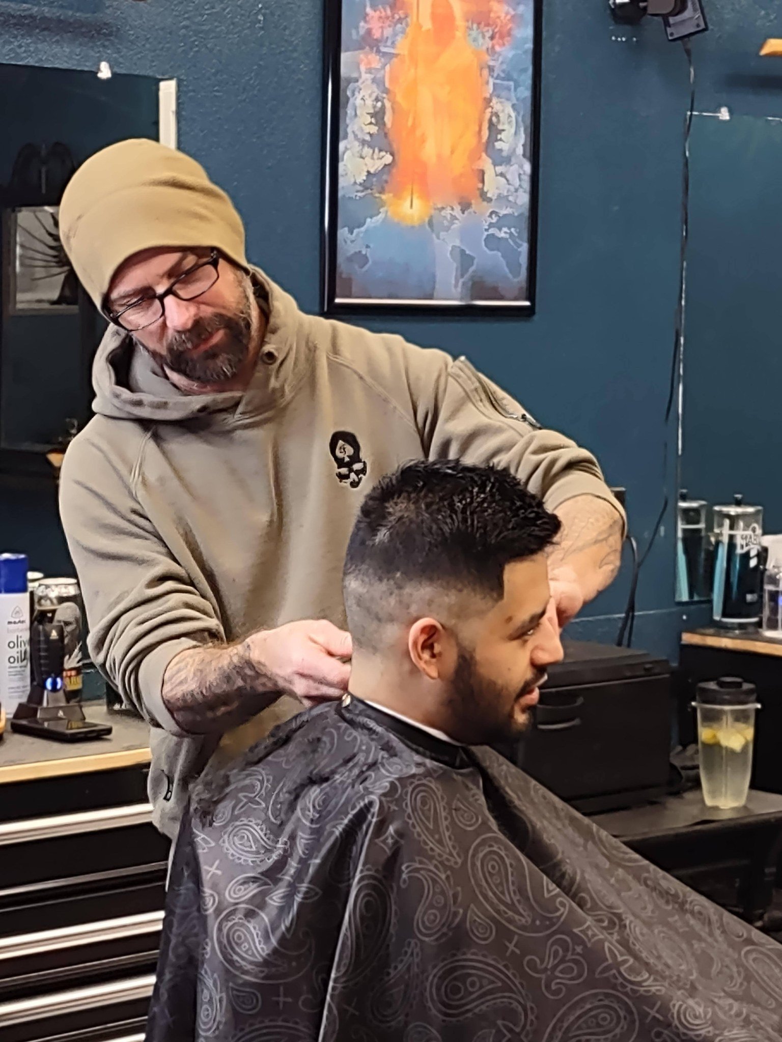 Barber giving a haircut to a young man in a barbershop with a colorful abstract painting in the background.