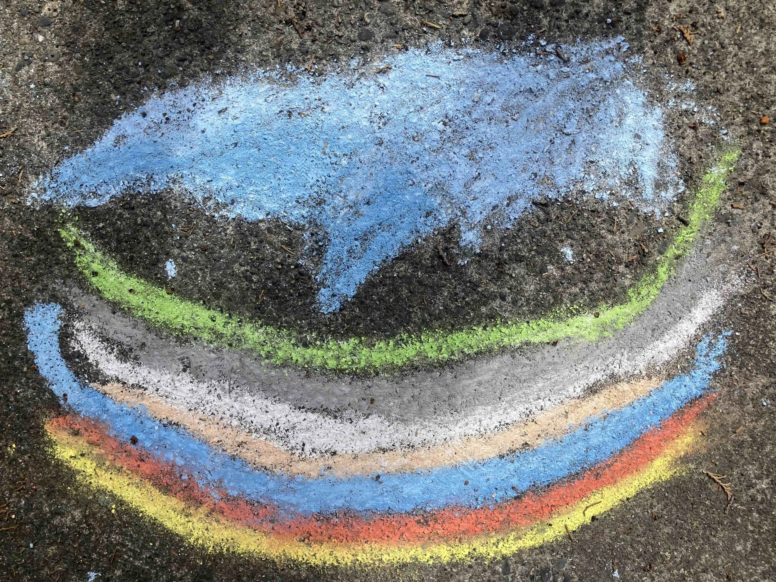 Colorful chalk drawing of a rainbow on an outdoor sidewalk.