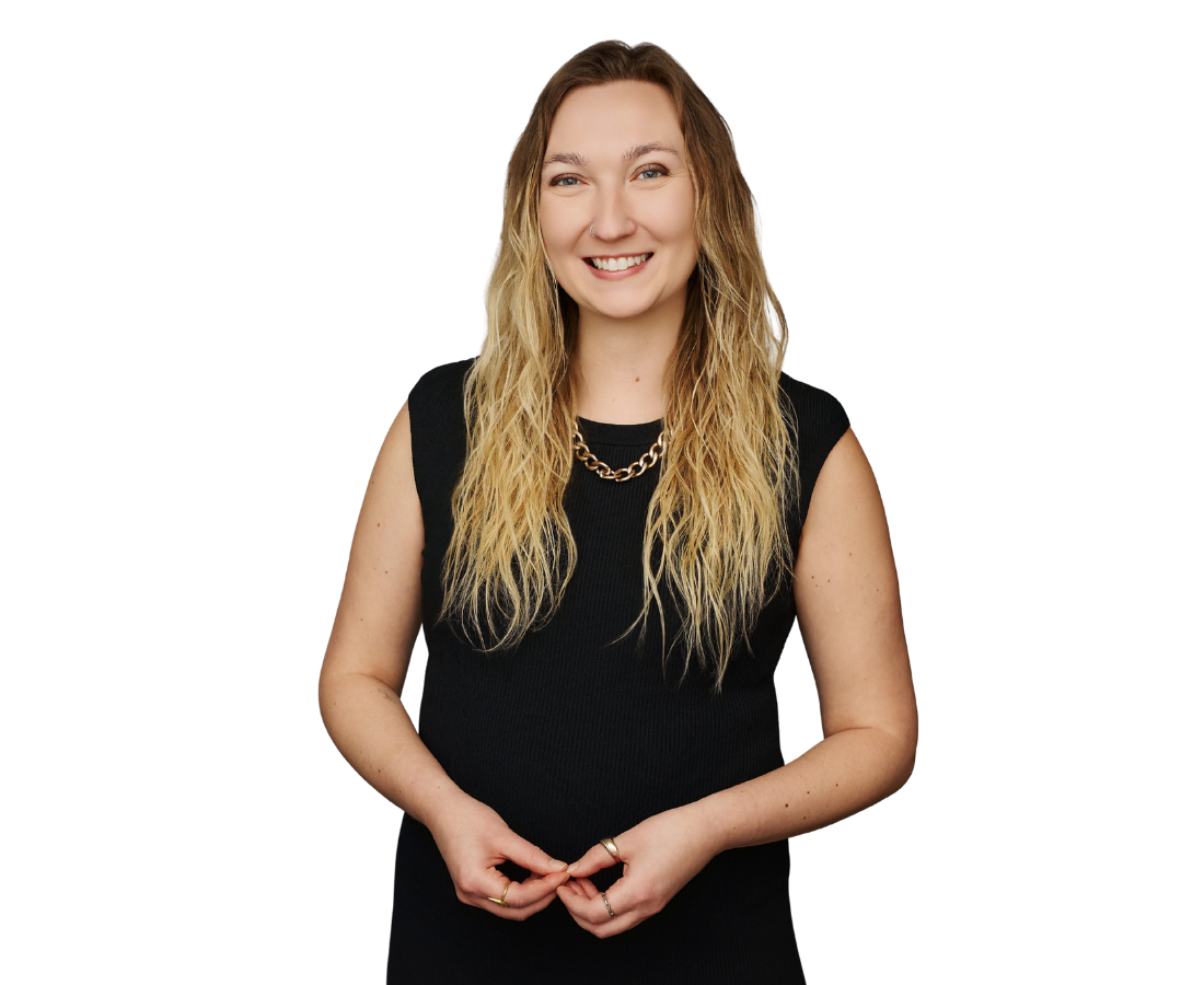 A smiling woman with long blonde hair wearing a black sleeveless top and gold chain necklace, standing against a dark background with a purple accent.
