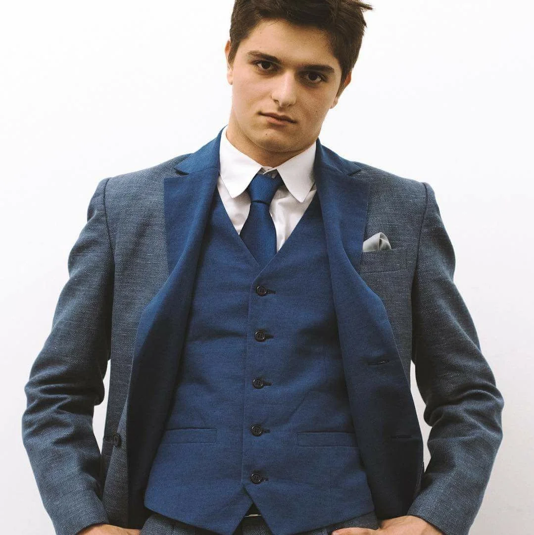 Young man in a blue suit with a white shirt and blue tie, posing against a plain white background.