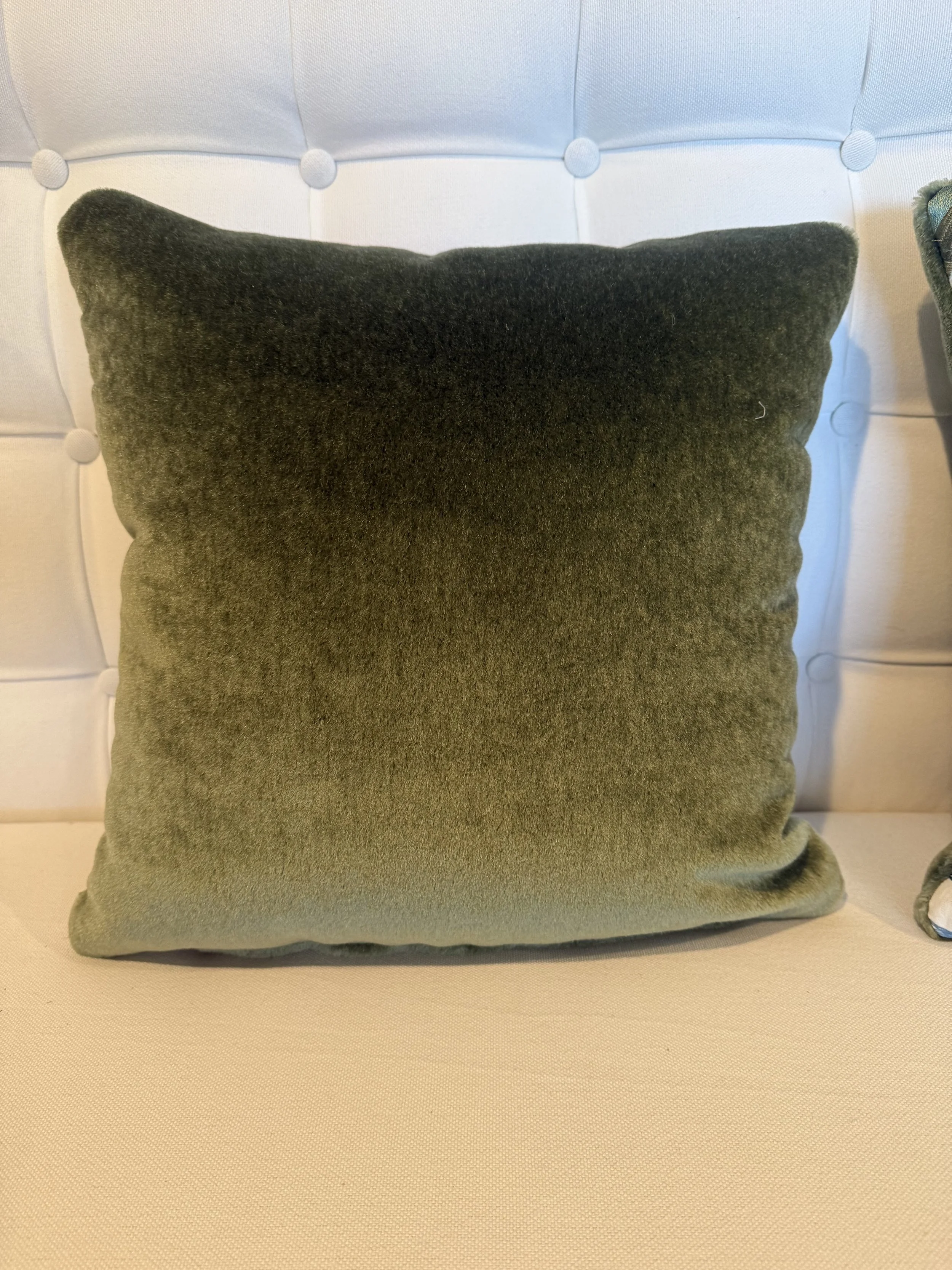 A green velvet cushion on a cream-colored tufted chair with white buttons.