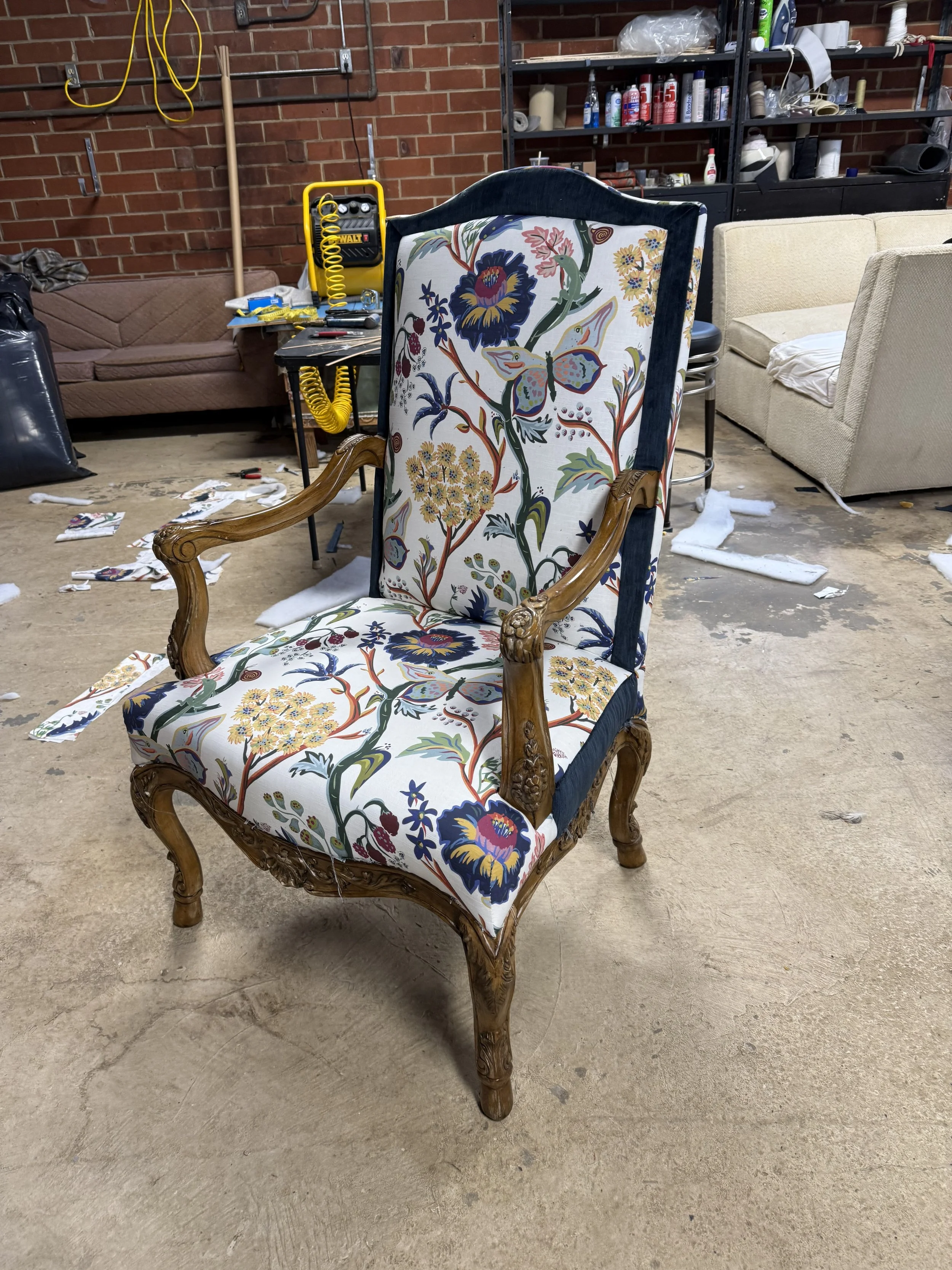 A vintage armchair with floral fabric upholstery and ornate wooden carved legs and arms in a workshop or storage area.