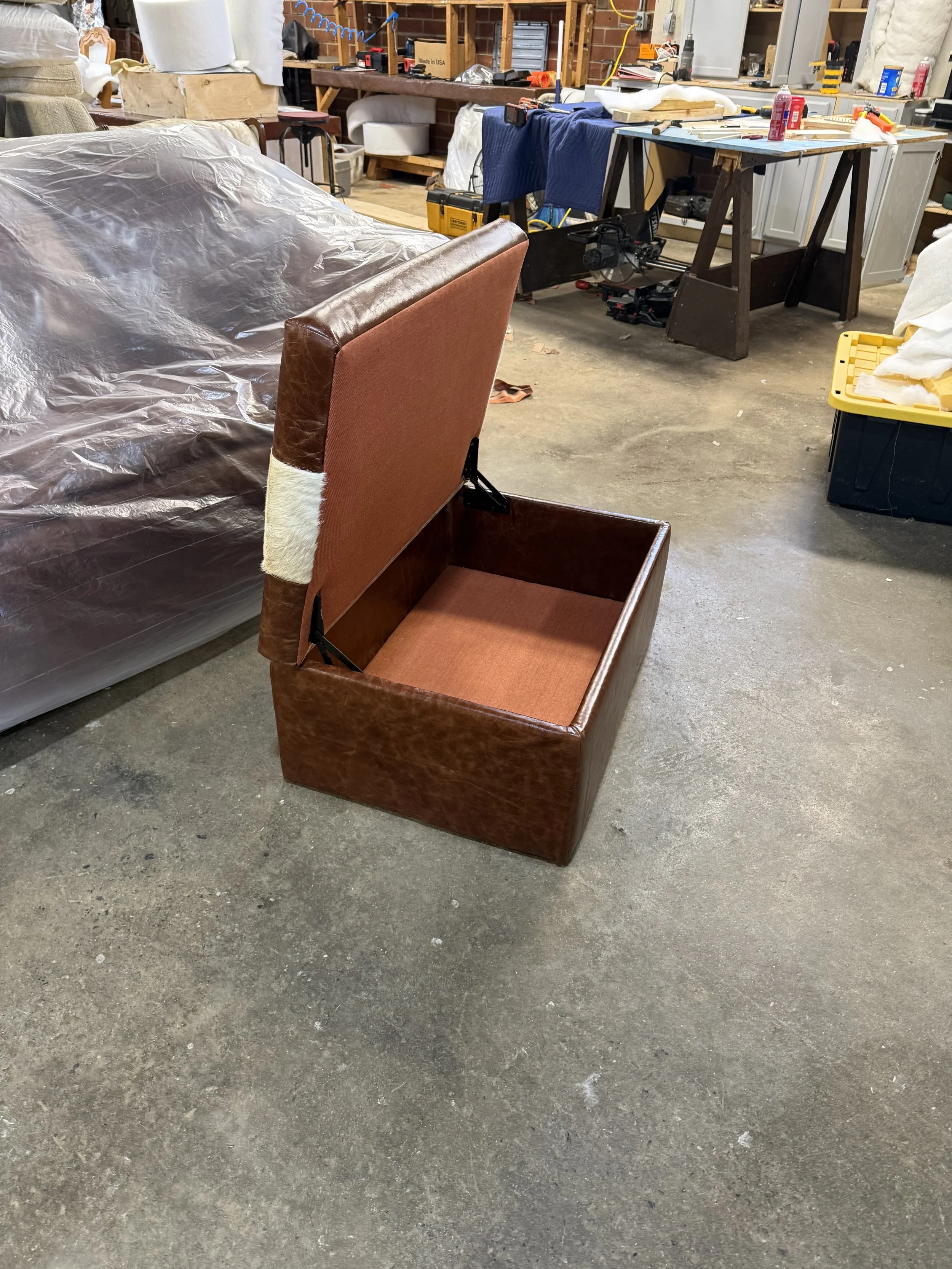A workshop with a partially disassembled vintage armchair and a plastic-covered sewing machine on a wooden table in the background.