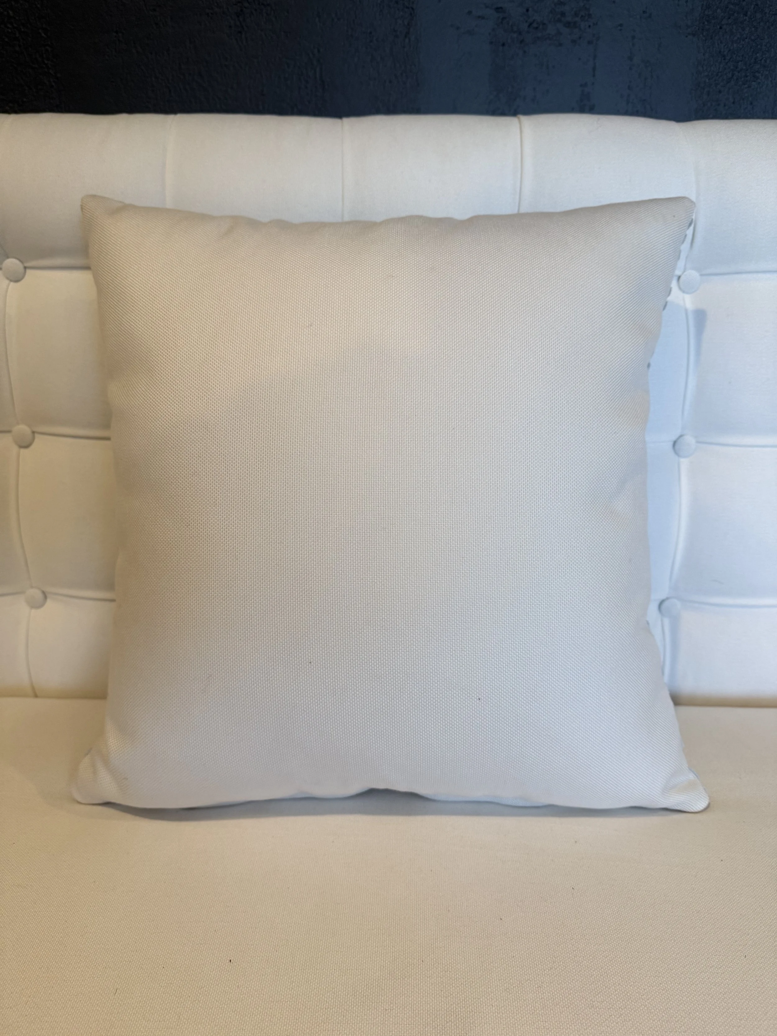 Cream-colored cushioned headboard with a matching pillow against a dark blue wall.