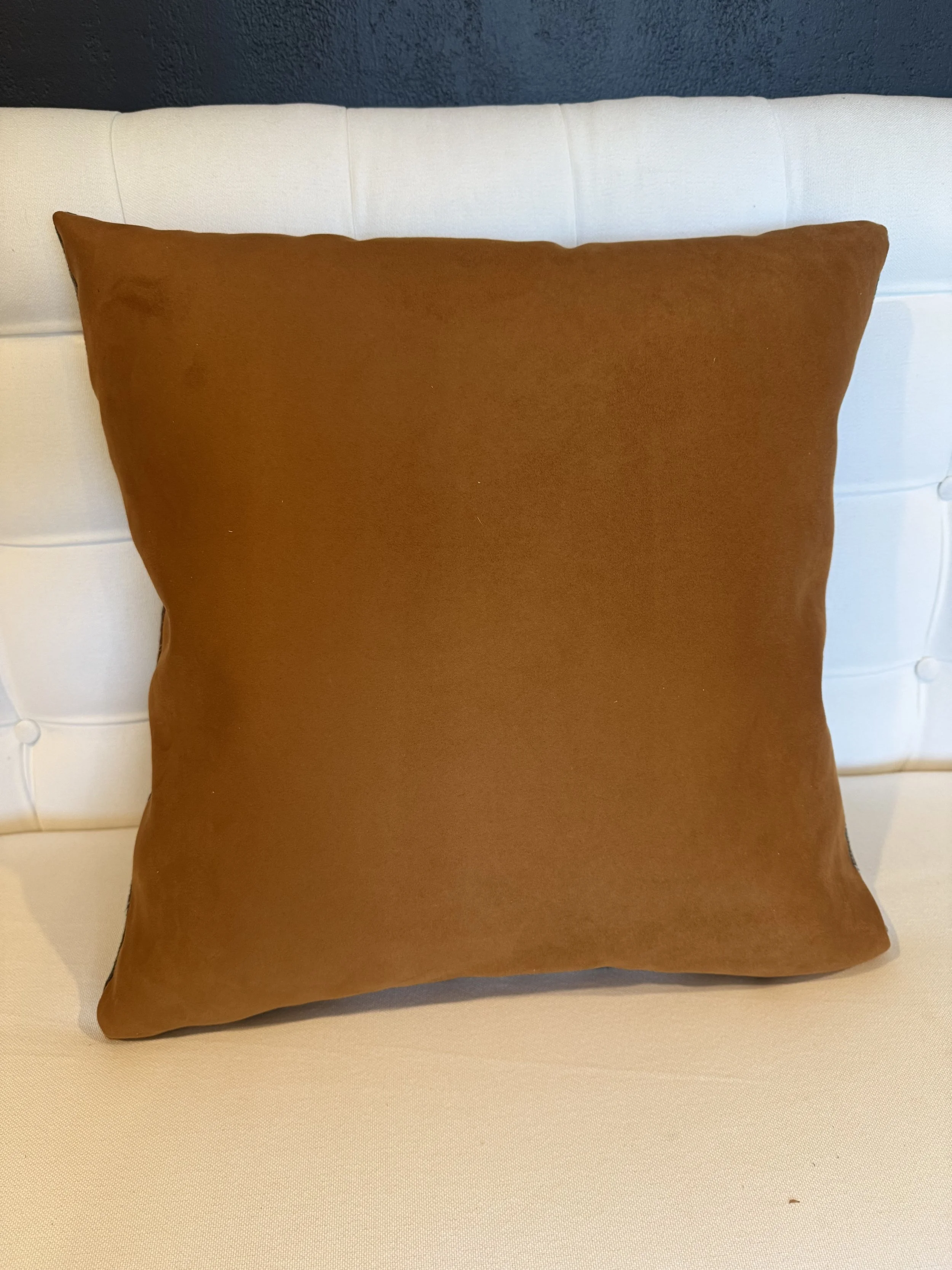 Brown decorative pillow on a white tufted bed with a dark wall behind.