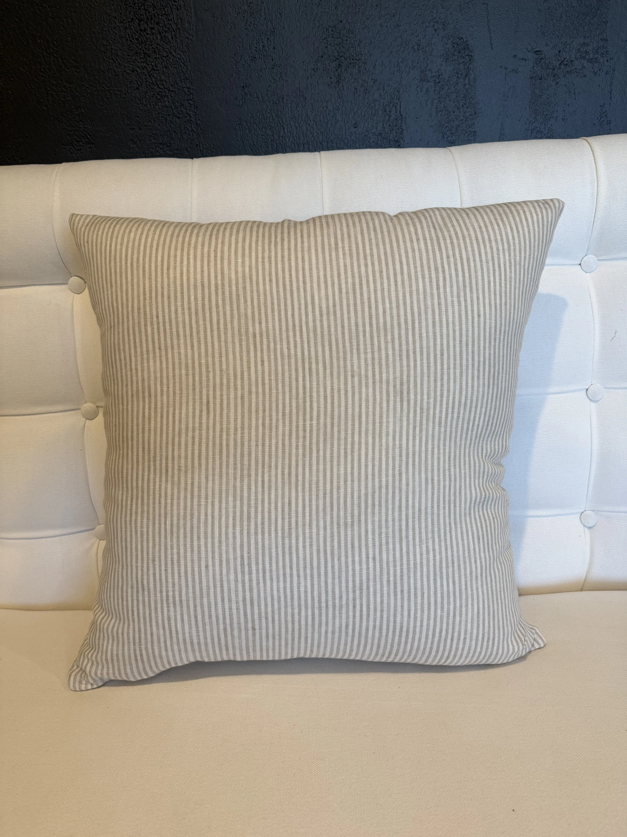 A beige upholstered bed with a beige and white striped pillow on it, set against a dark textured wall.