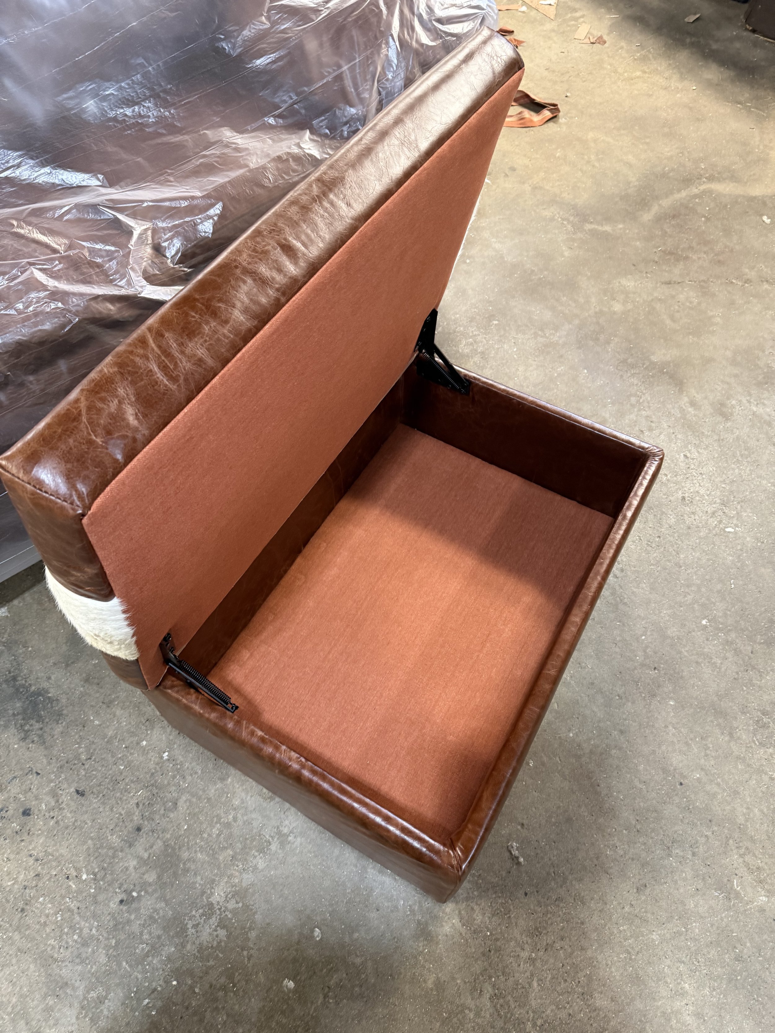 A brown upholstered cubed chair with a straight back, placed on a concrete floor. There's a cup holder on the side, and a plastic cover on the seat, indicating it's new or protected.