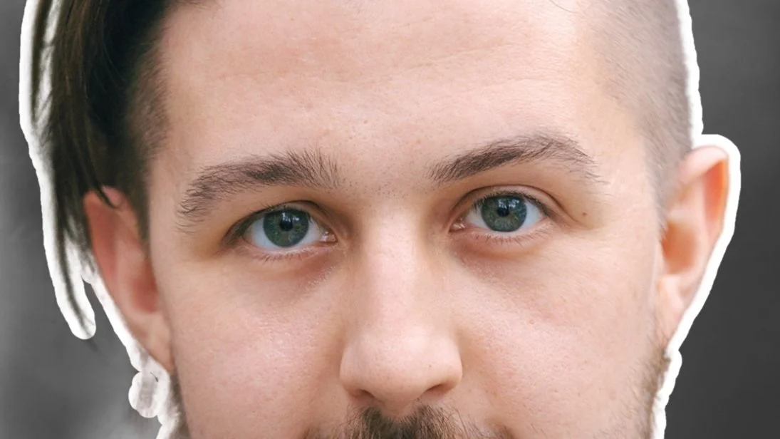 Close-up of a young man's face with blue eyes, light skin, and dark hair.