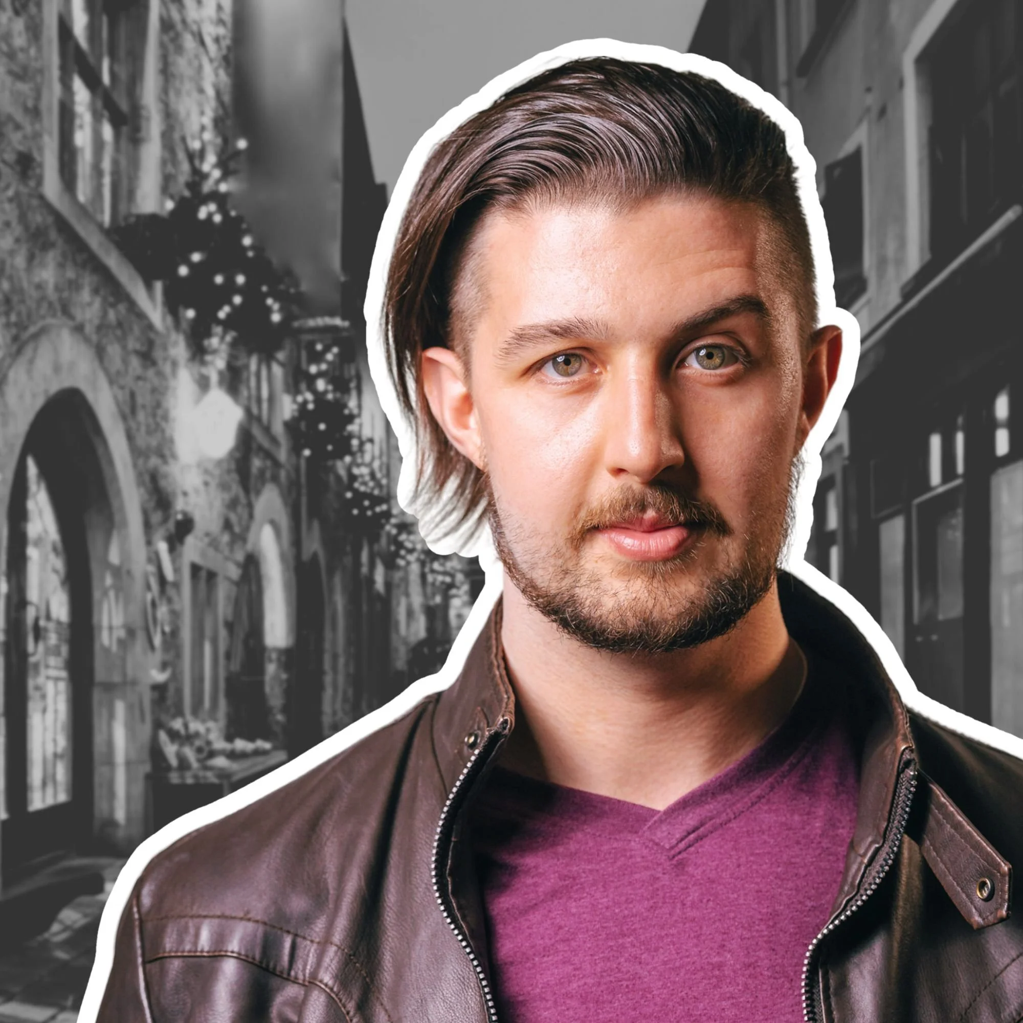 A young man with styled hair and a beard wearing a leather jacket over a maroon t-shirt, standing on a city street with buildings and Christmas lights in the background. Kai Mann-Robertson