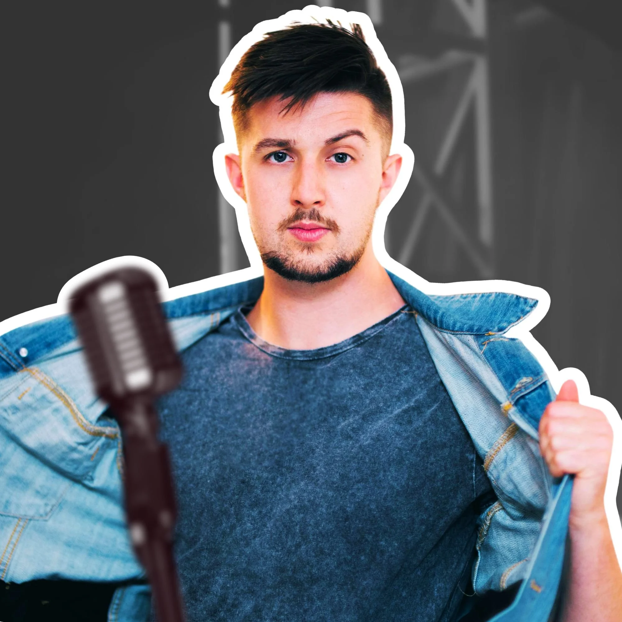 Kai Mann-Robertson Young man with dark hair and facial hair, wearing a dark gray t-shirt and denim jacket, standing in front of a microphone.