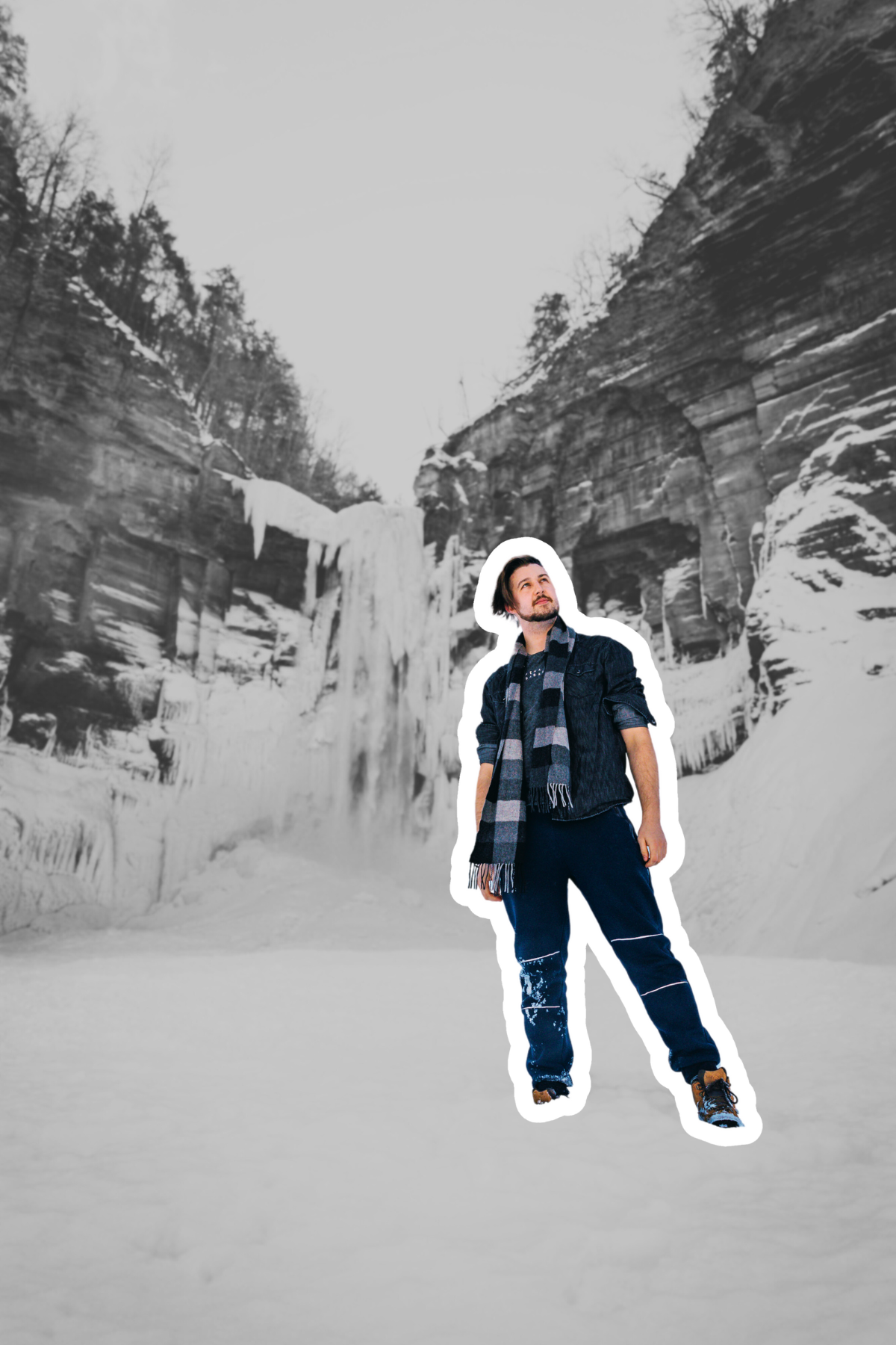 Kai Mann-Robertson A man stands on snow in front of a frozen waterfall and icy cliff walls in a winter landscape.