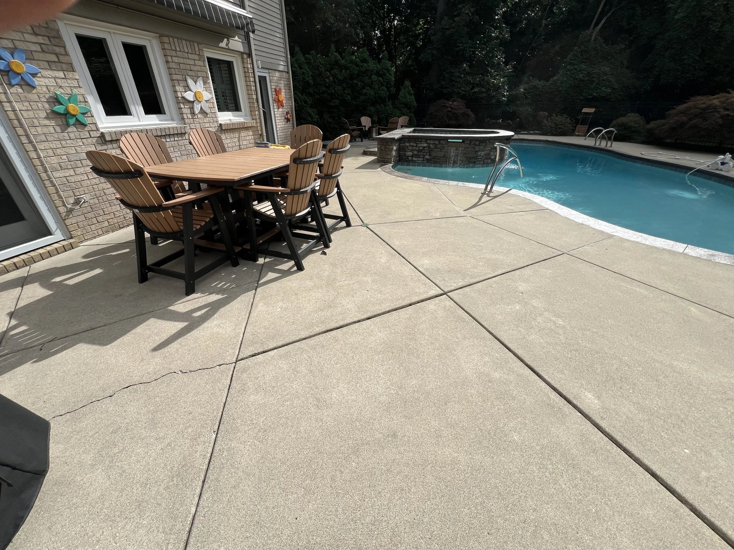 Backyard patio with a dining table and chairs near the house, swimming pool, and hot tub with trees in the background.