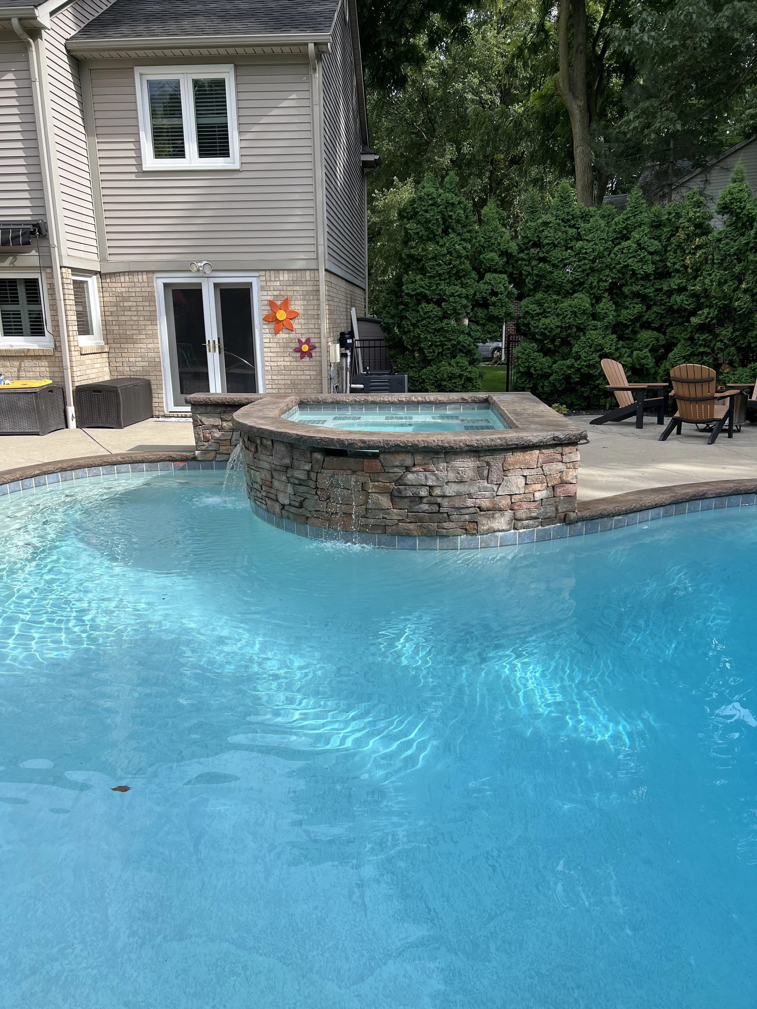 Backyard with a swimming pool and hot tub, patio chairs, and a house with decorative flower wall hangings.