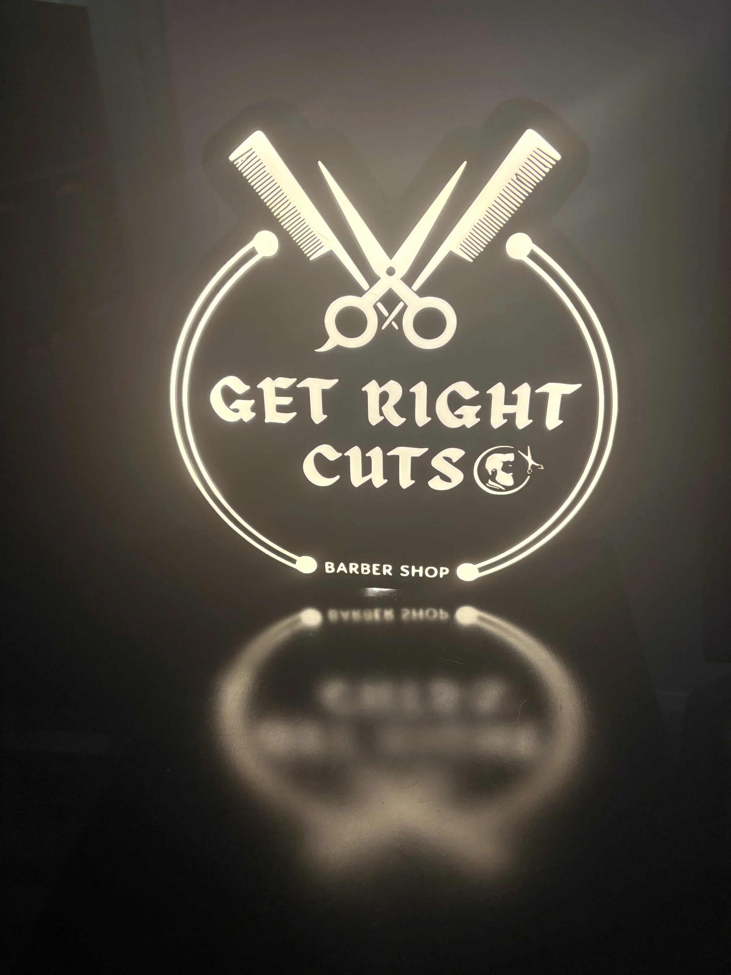Backlit sign for a barbershop with scissors, combs, and text 'Get Right Cuts' and 'Barber Shop'.