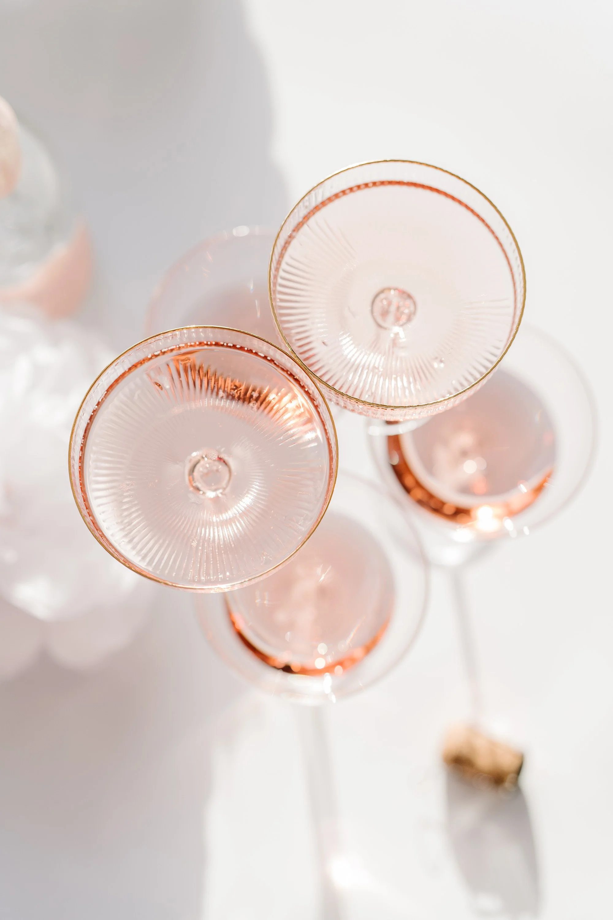 a flatlay of pink cocktail glasses on top of other ones on a white table