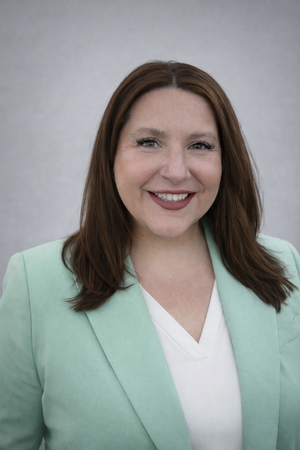 A headshot of Kim Cooper, with dark medium long hair and a mint-colored blazer with a white top
