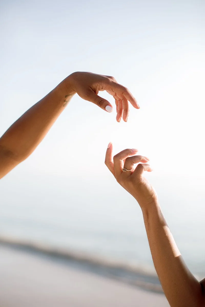 two women's arms in the image and are about to touch fingers where one arm is on top of the other hand