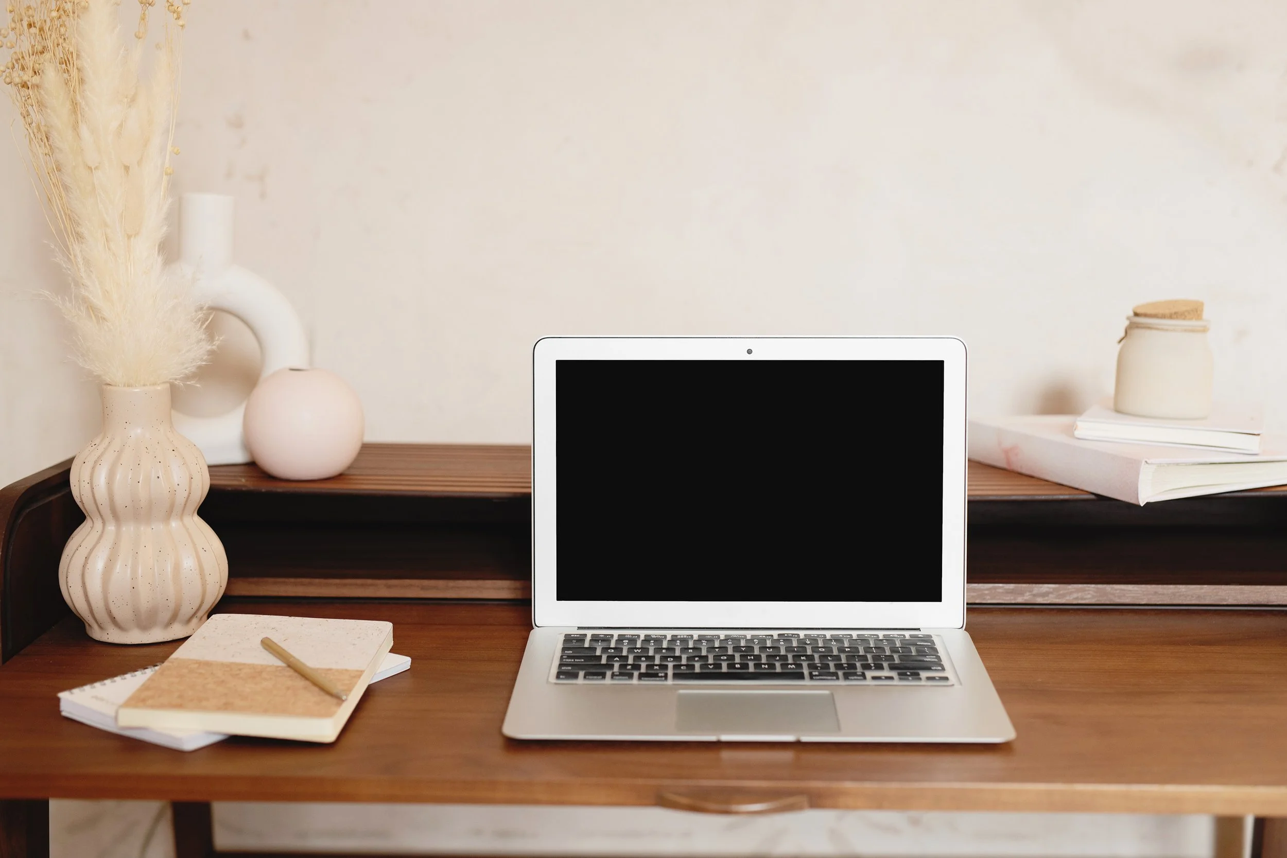 A brown desk with ceramic vases on the left side and 2 journals stacked on top of each other while a laptop is opened on the other side