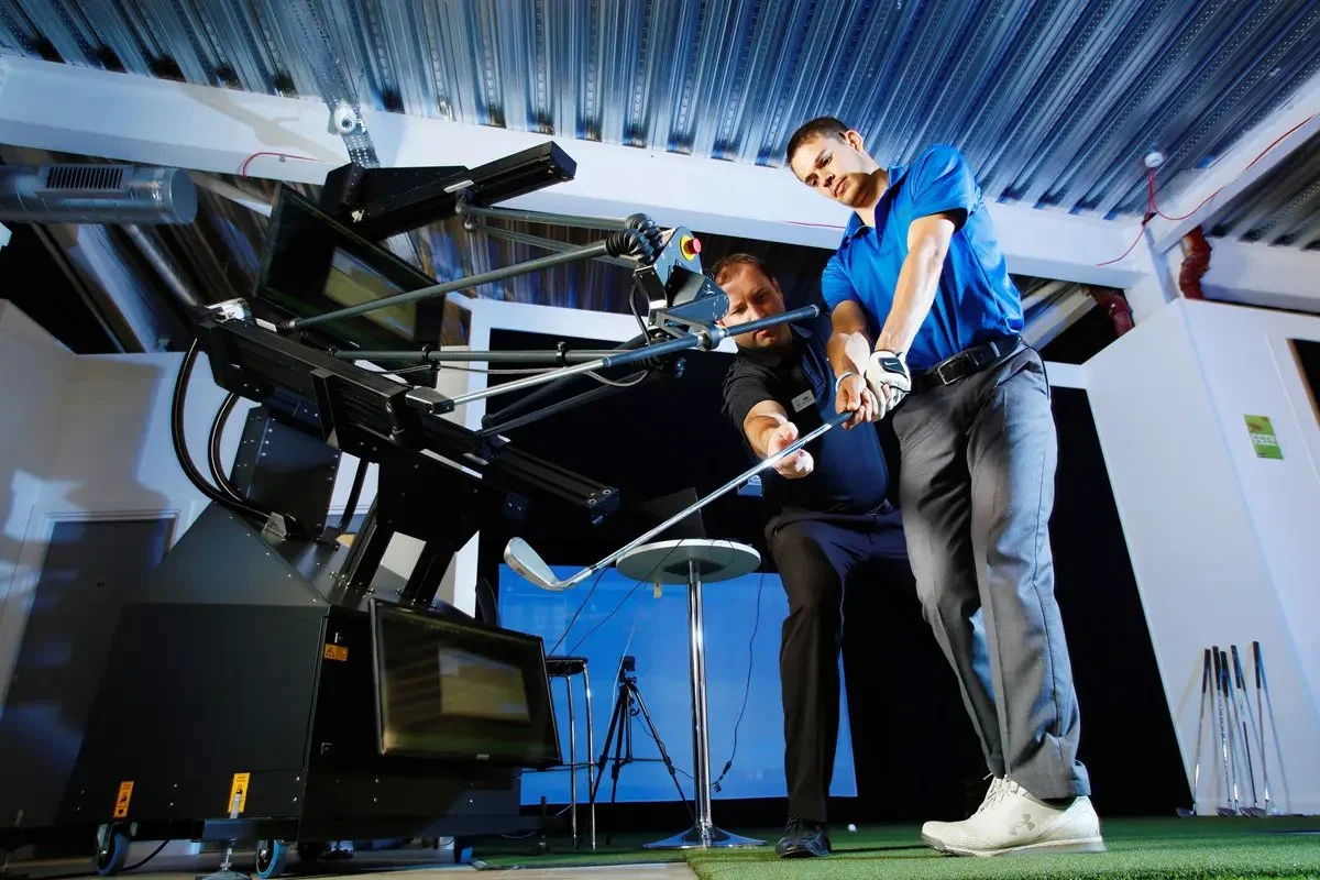 Two men practicing golf on a high-tech golf simulator, with a screen displaying a virtual golf course.