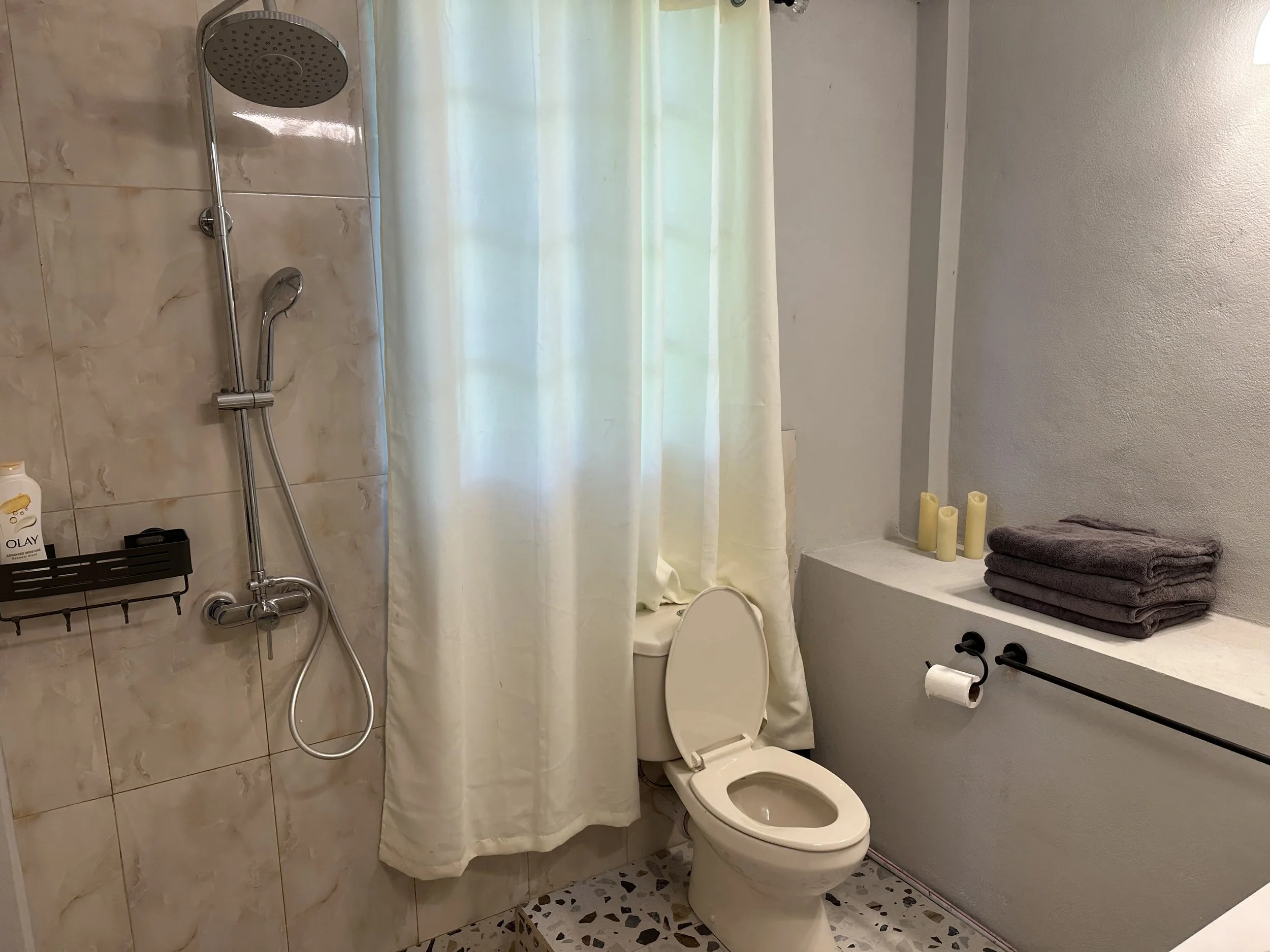 Bathroom with shower area, toilet, towels, candles, and a curtain.