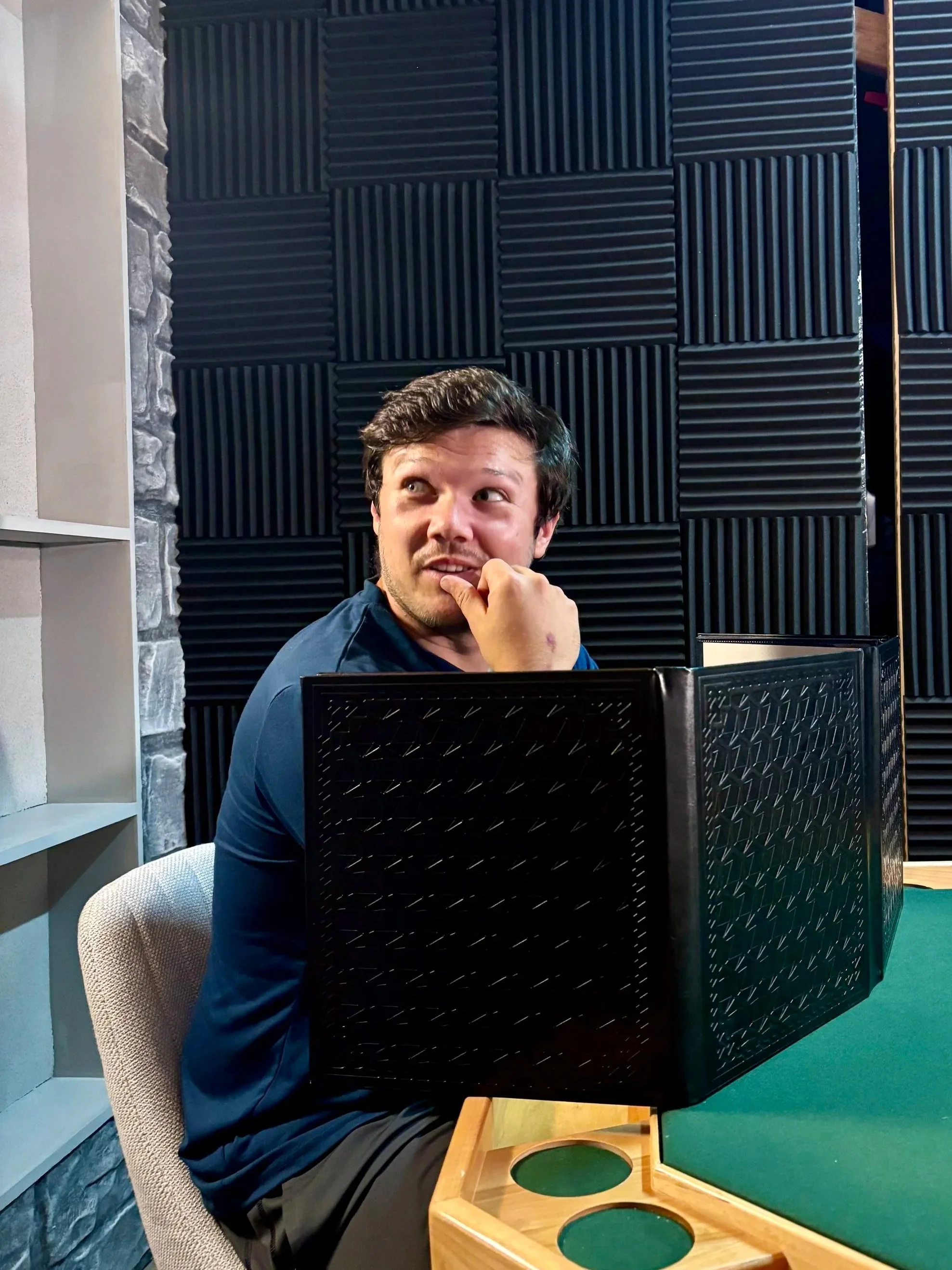 Man sitting at a table with a green surface, thinking, in a room with black acoustic foam panels on the wall.