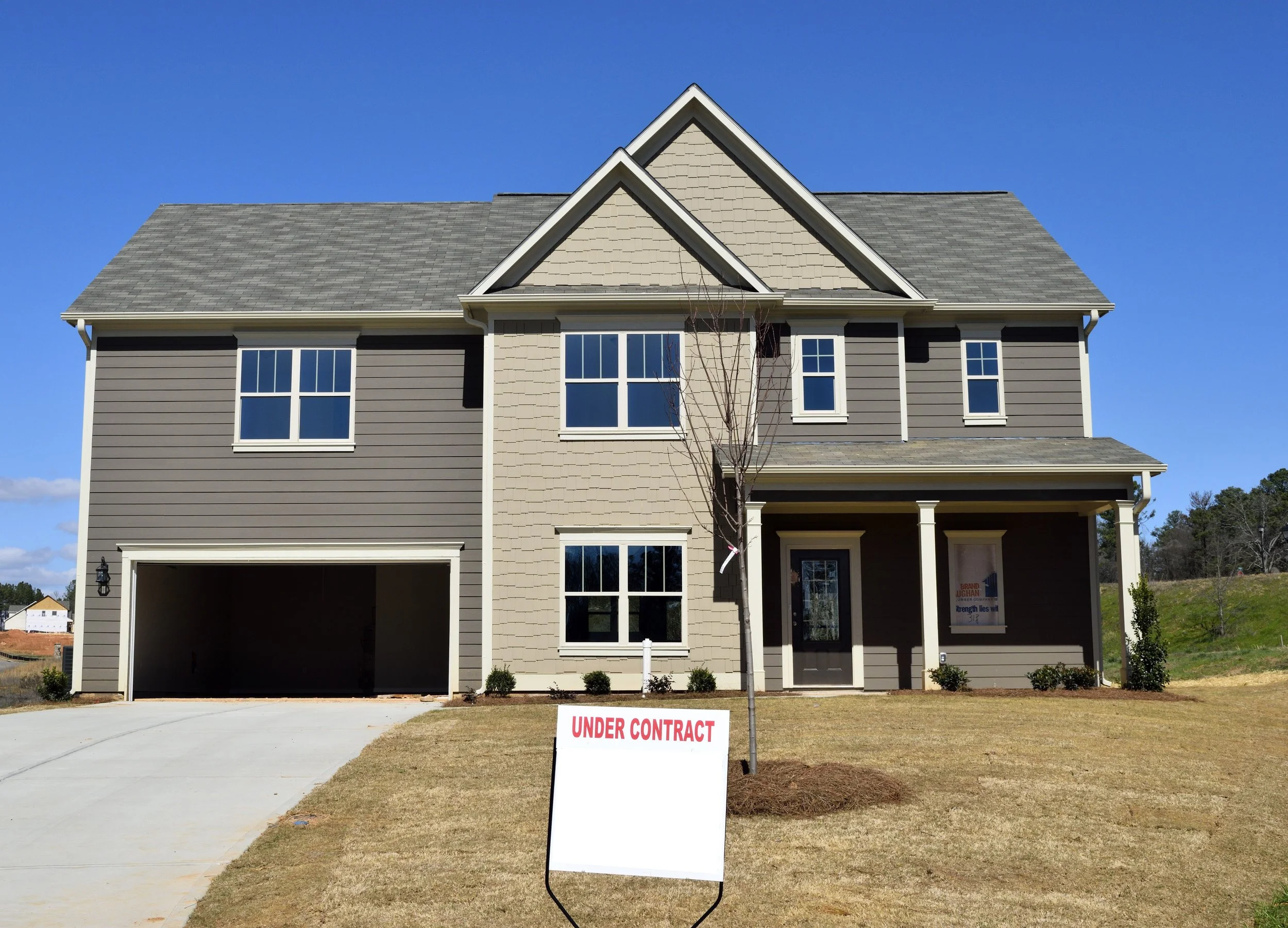 New two-story house with gray and beige siding, front porch, and an 'Under Contract' sign in the yard.