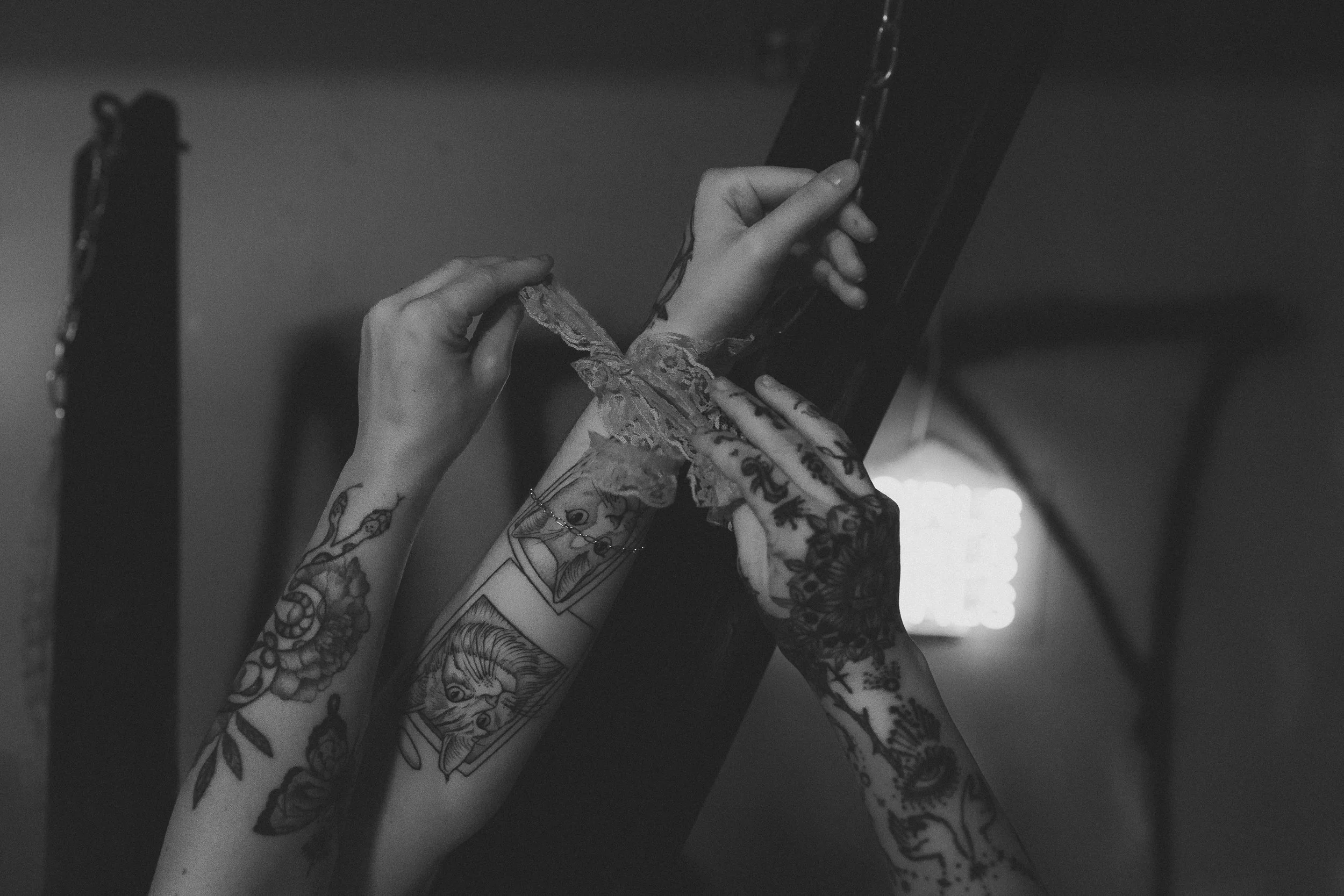 Close-up of multiple tattooed arms and hands holding and pulling a black photo frame with a lace cloth.