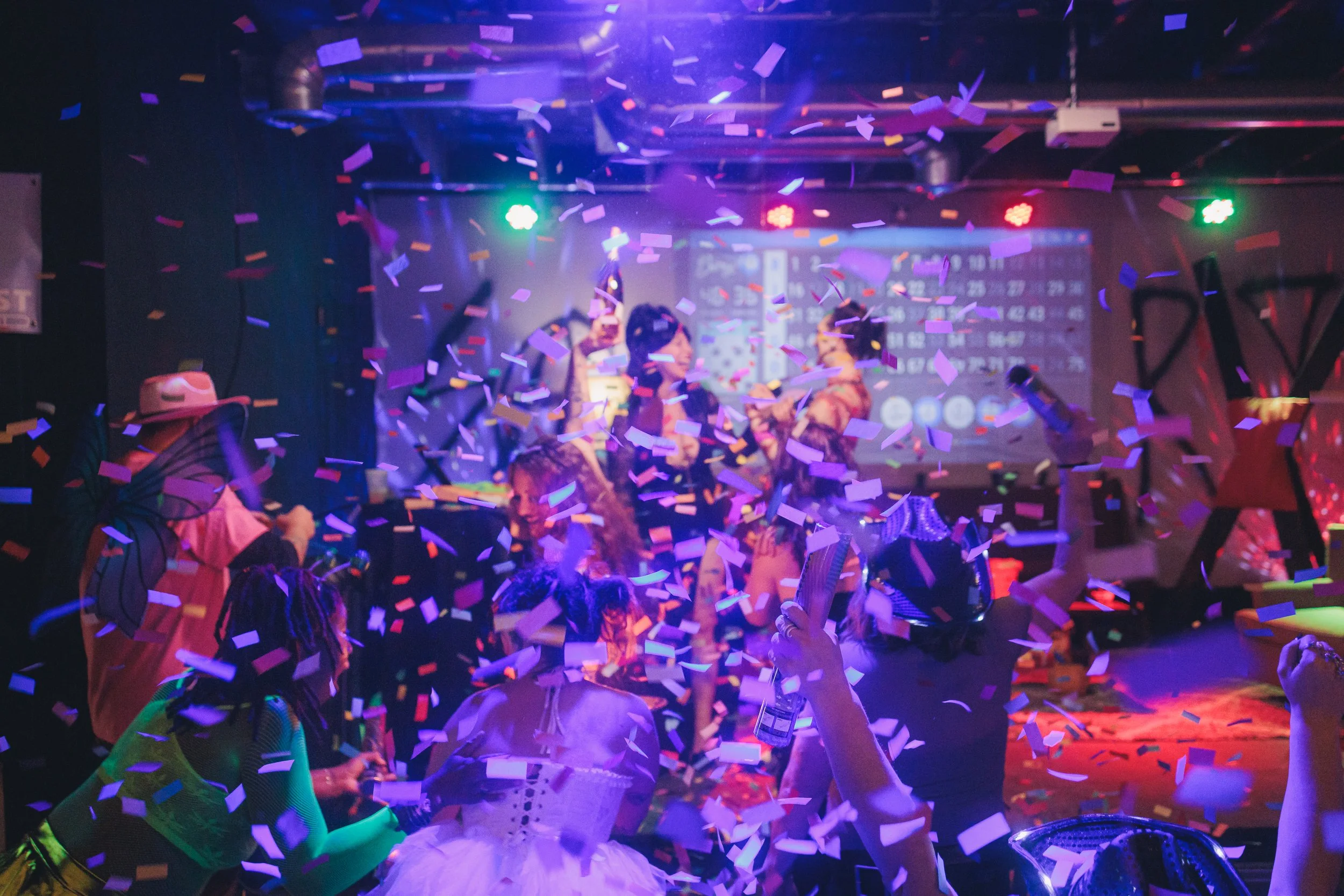 People at a celebration or party with colorful confetti falling, a dark background, and bright lights.