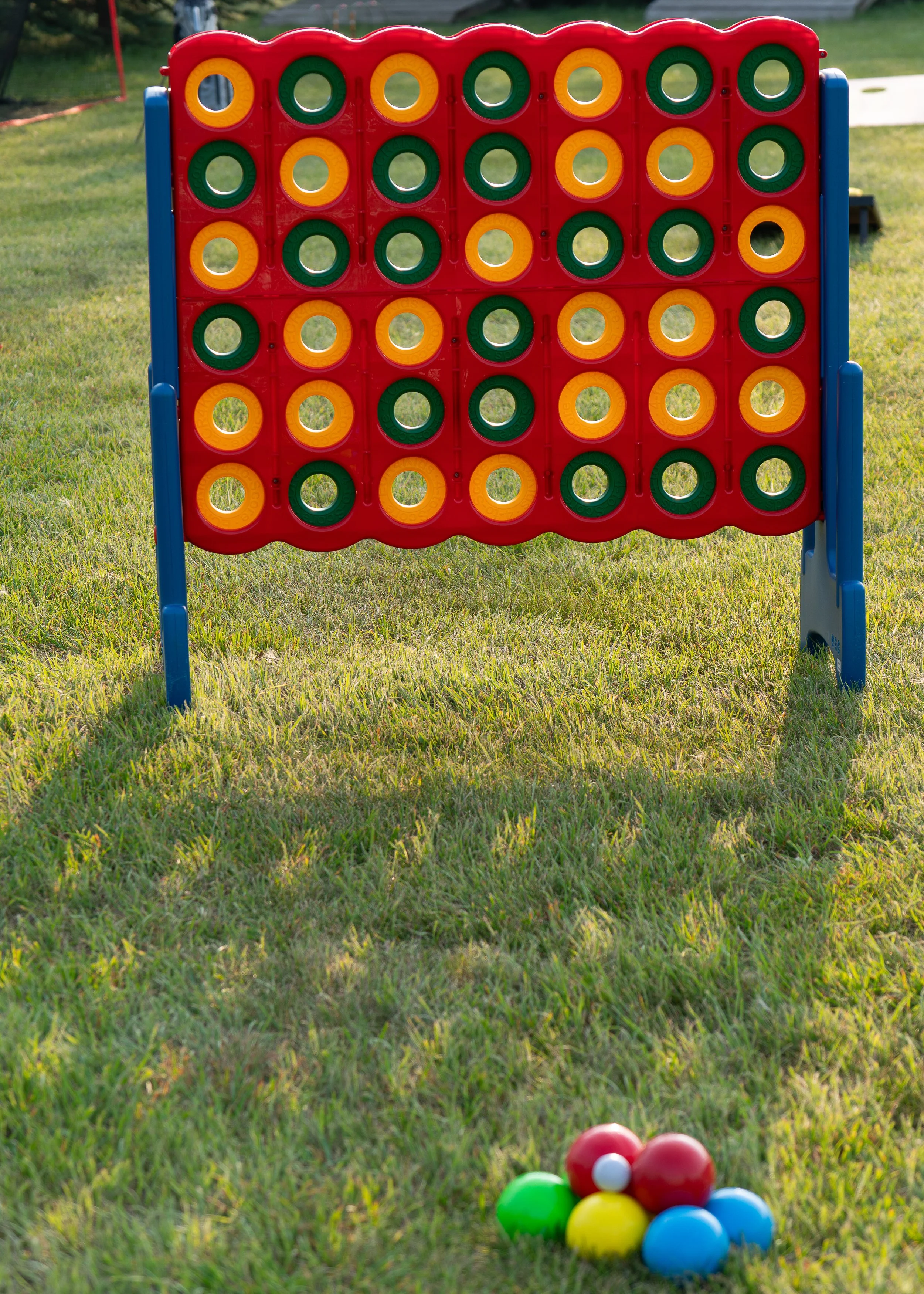 A large outdoor Connect Four game set up on grass with multicolored balls in front of it.