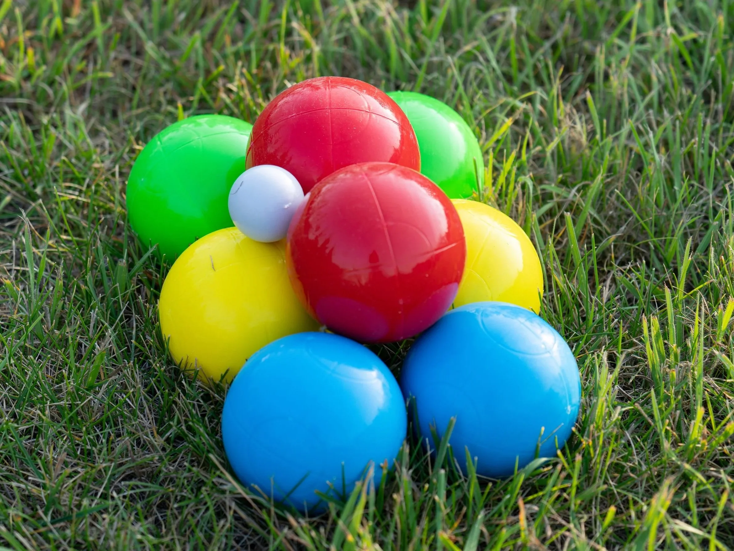 Colorful plastic balls in red, green, yellow, blue, and white, arranged in a cluster on green grass.